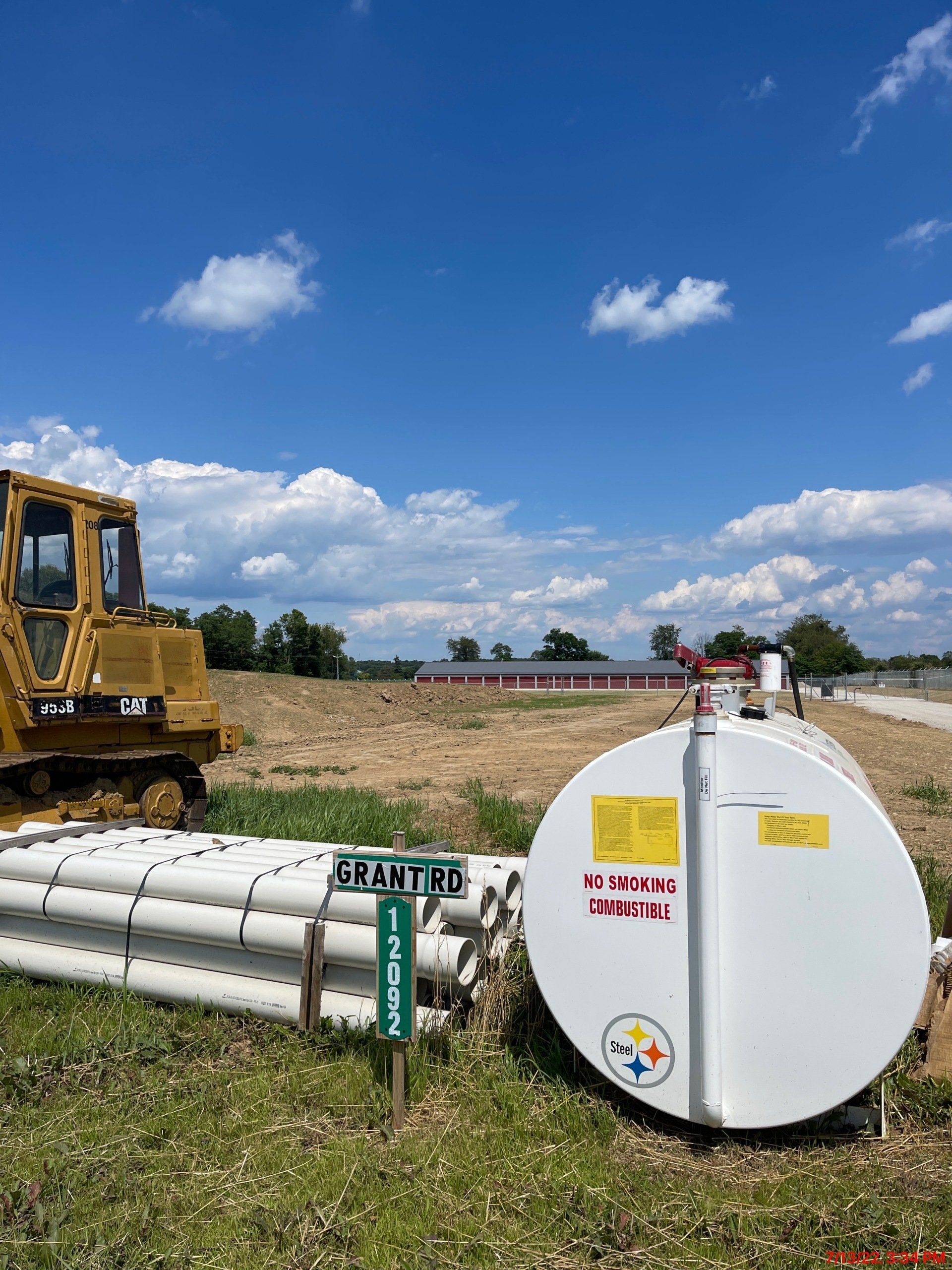 A bulldozer is parked in a field next to a large white tank.