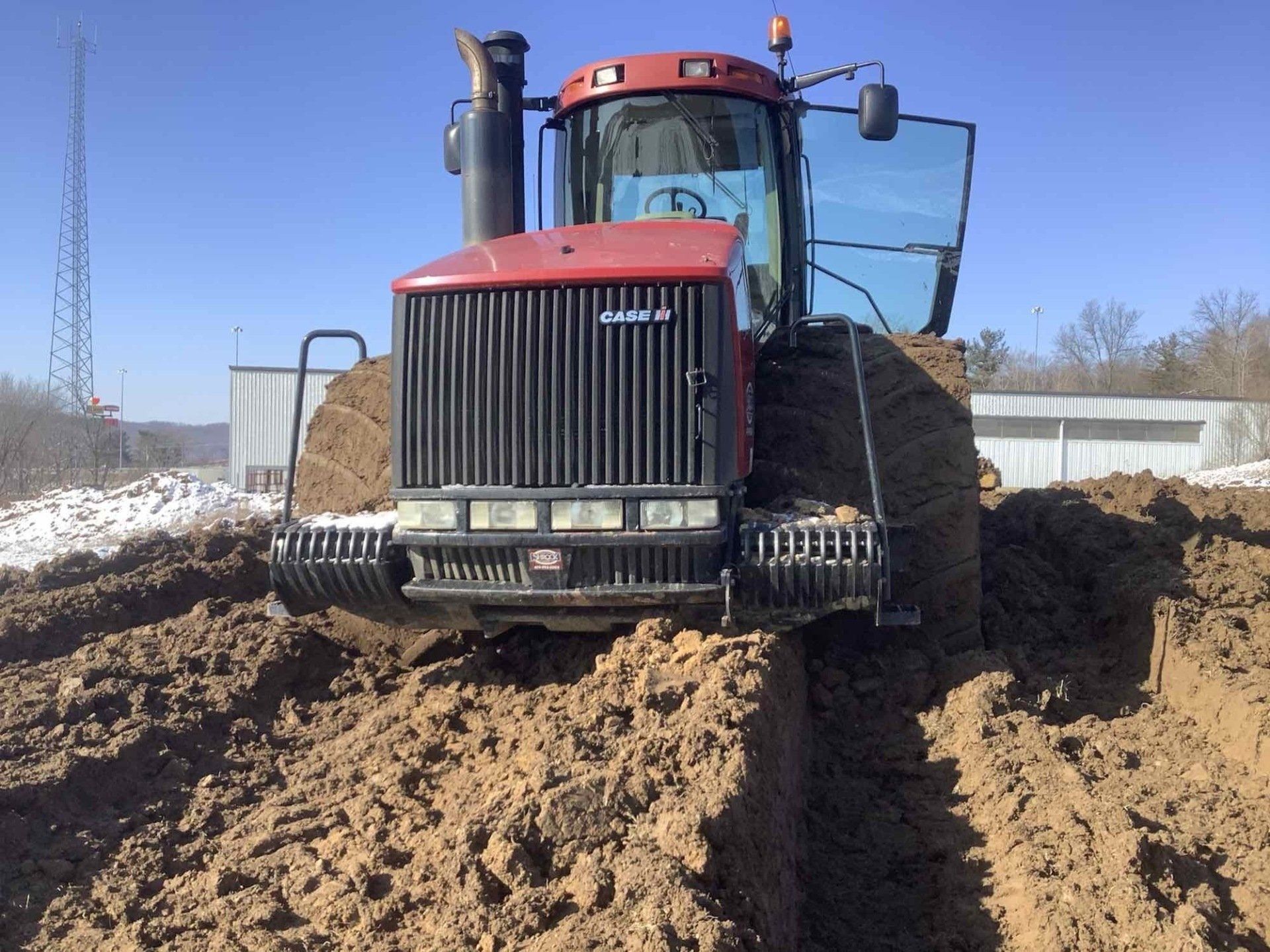 A red case tractor is driving through a muddy field