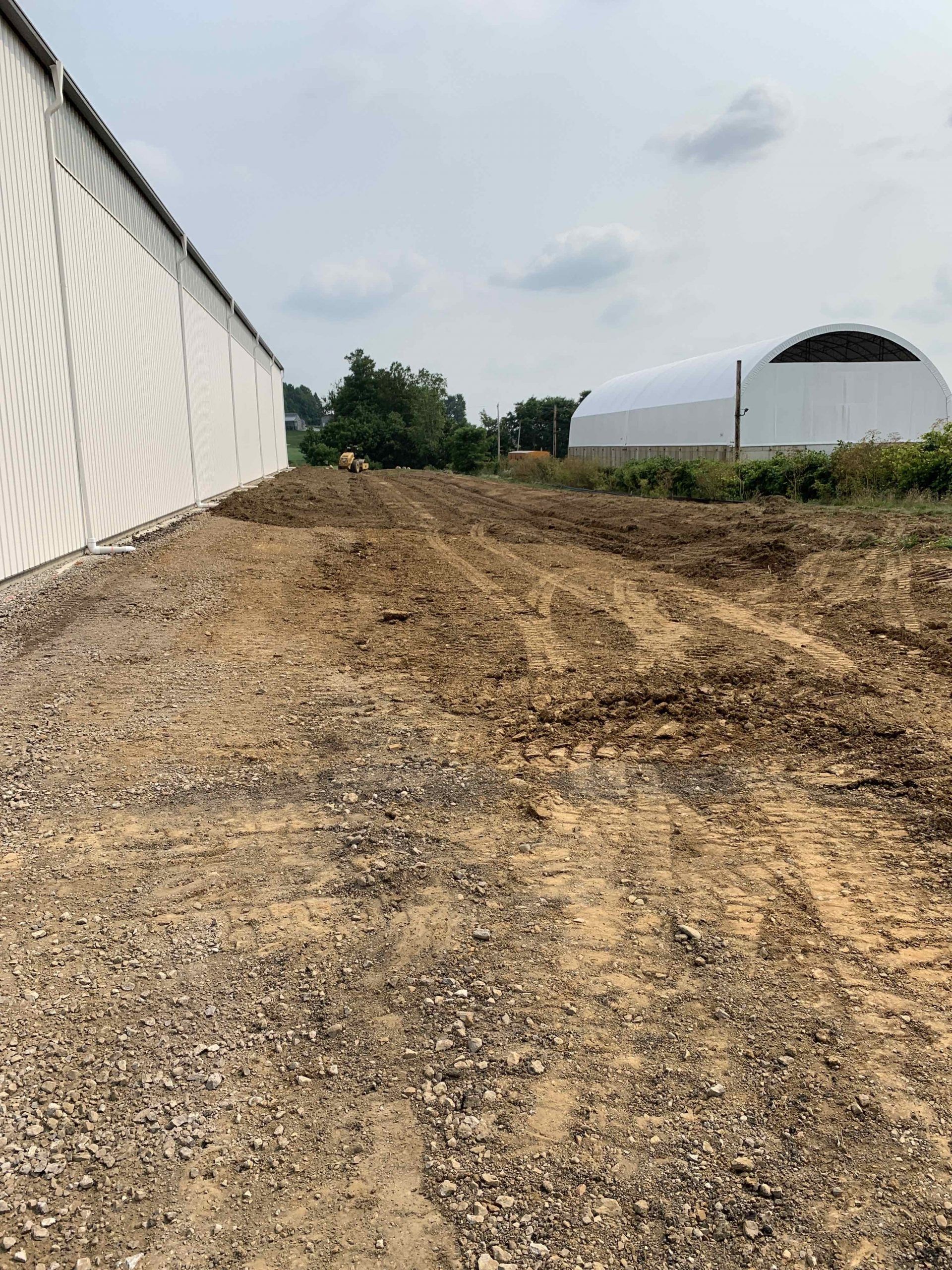 A dirt road leading to a building with a white building in the background.