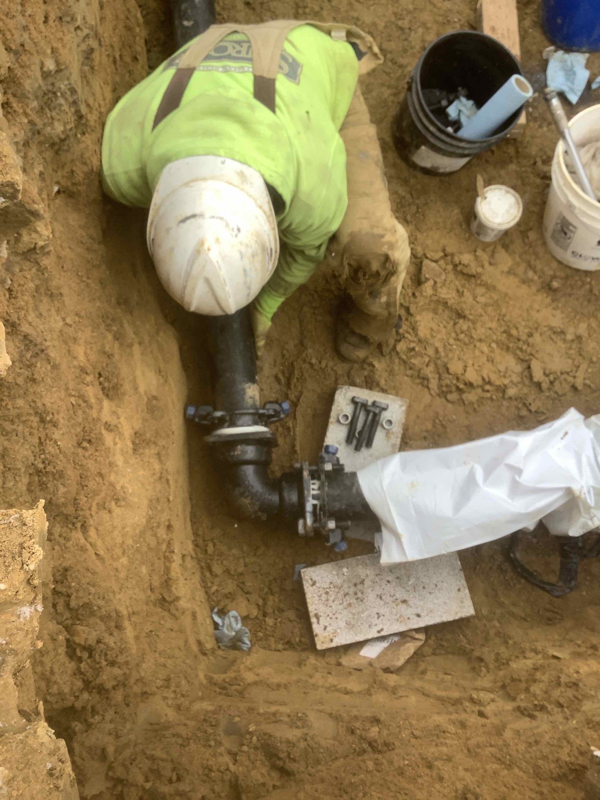 A man is working on a pipe in the dirt.