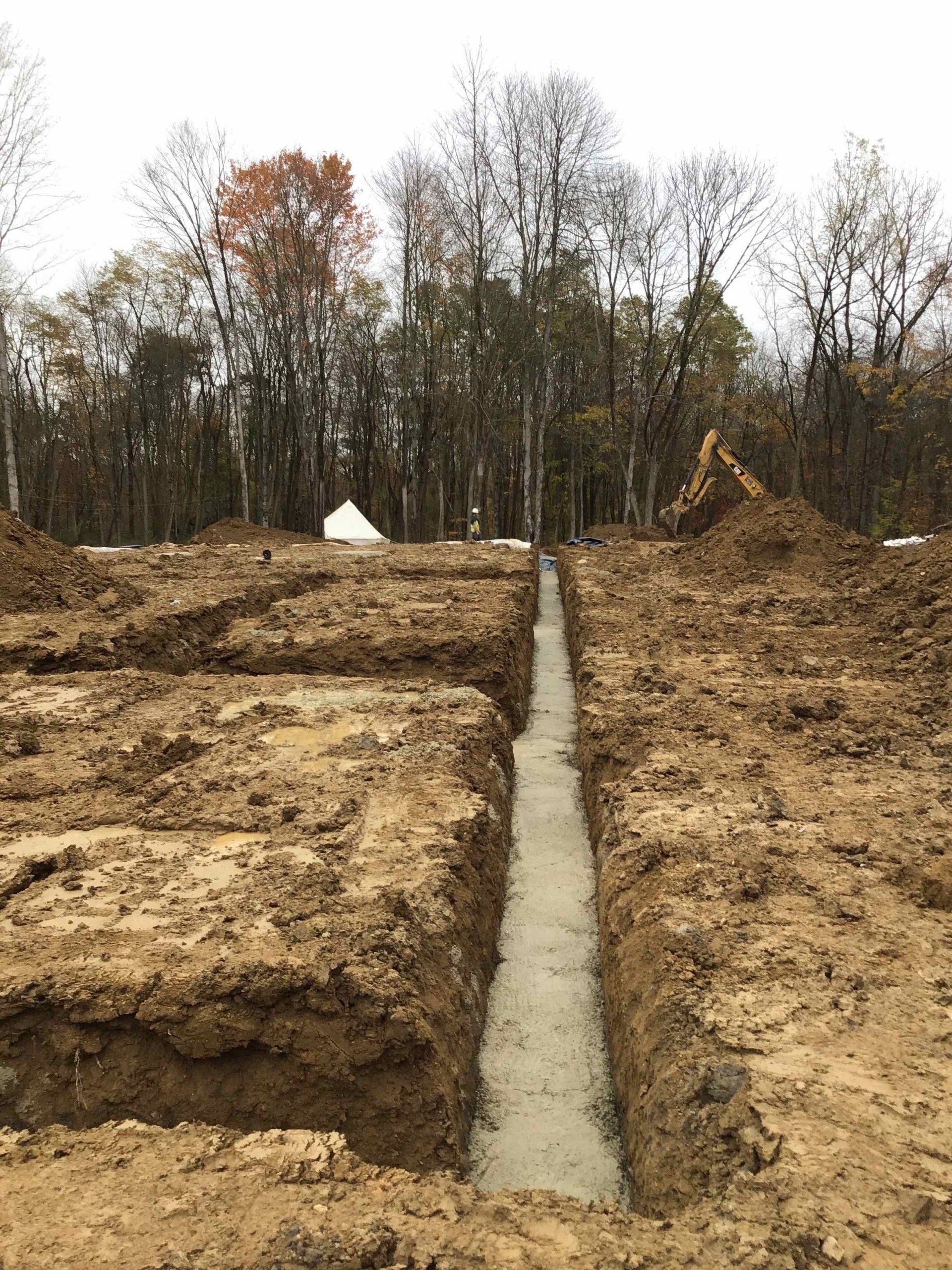 A construction site with a trench in the middle of it and trees in the background.