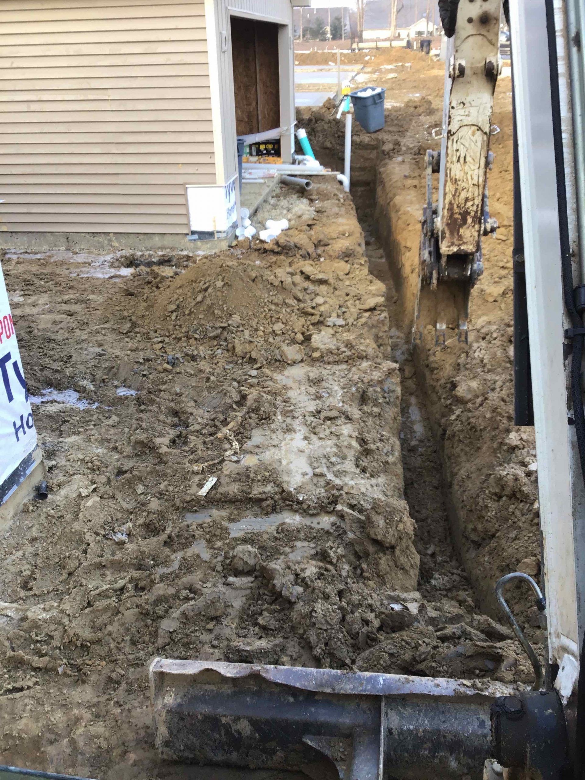 An excavator is digging a trench in the dirt in front of a house.