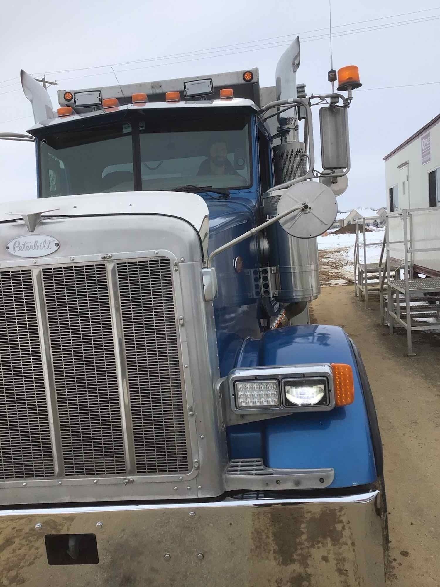 A blue semi truck is parked on the side of a dirt road.