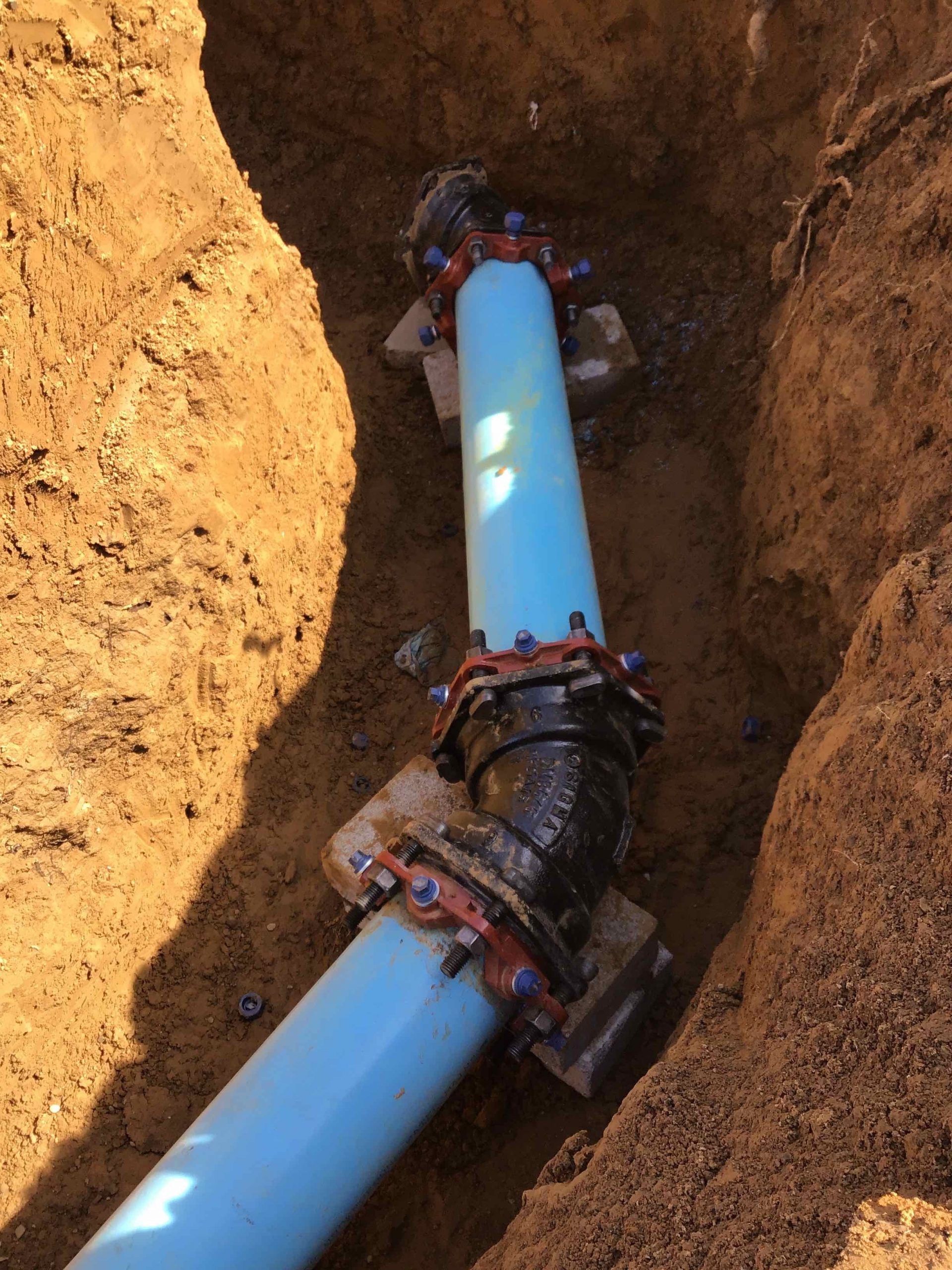 A blue pipe is laying in the dirt next to a black pipe