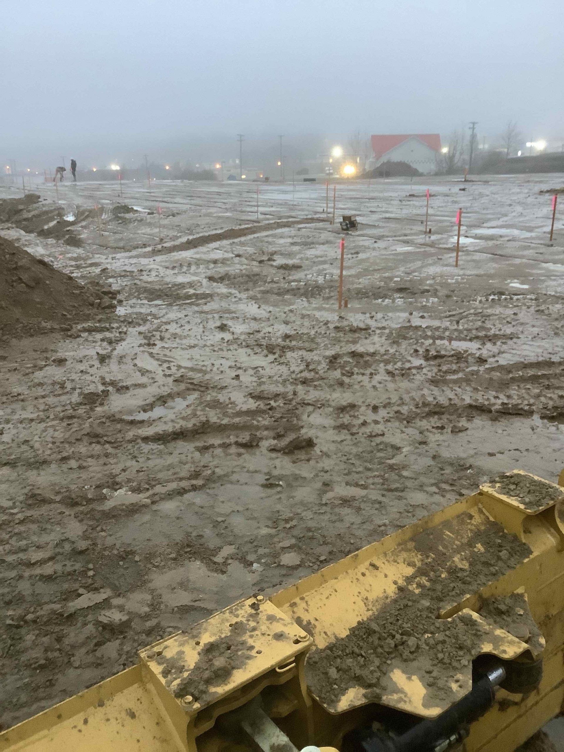 A muddy field with a tractor in the foreground and a building in the background.