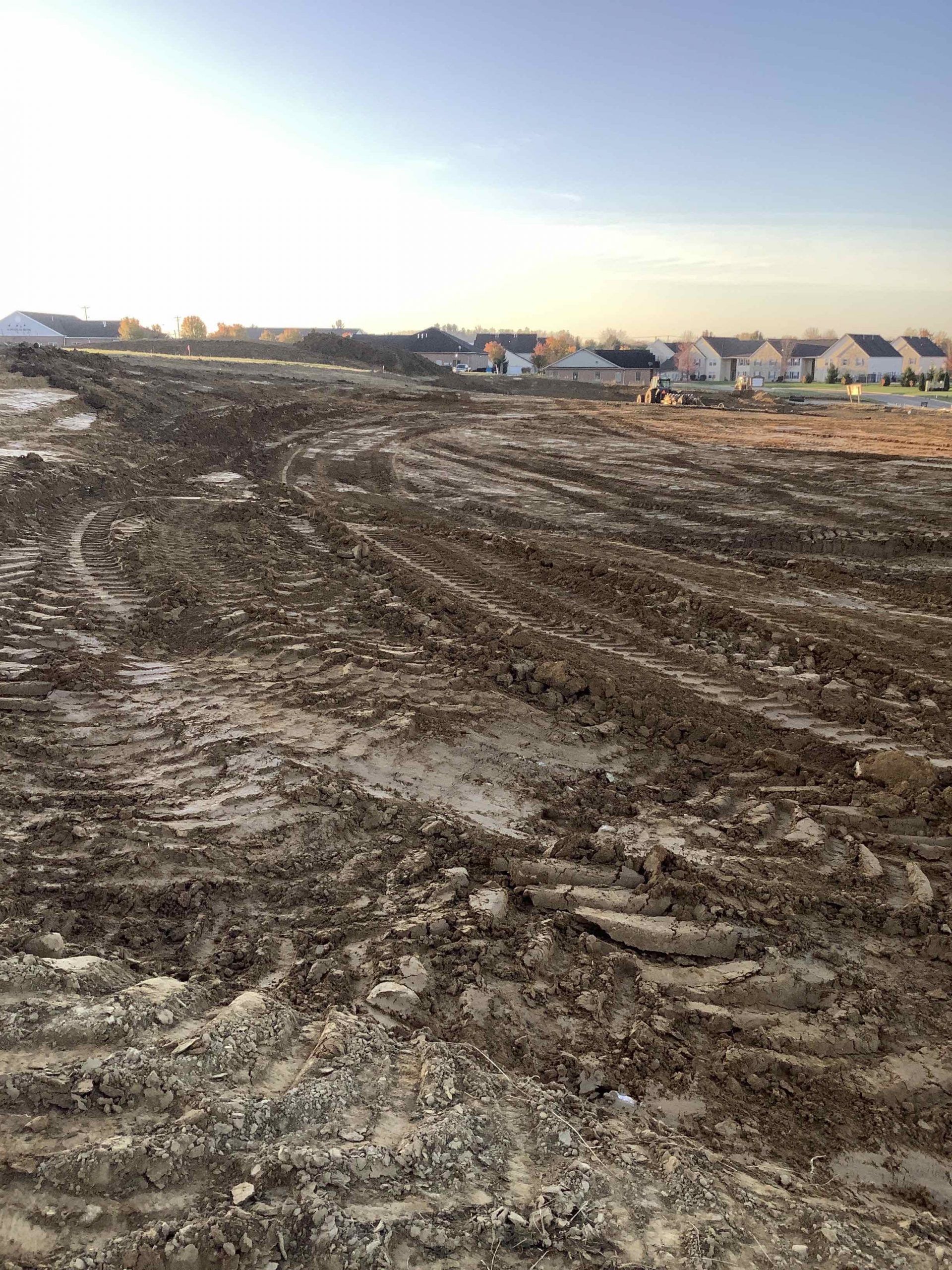 A large muddy field with houses in the background.