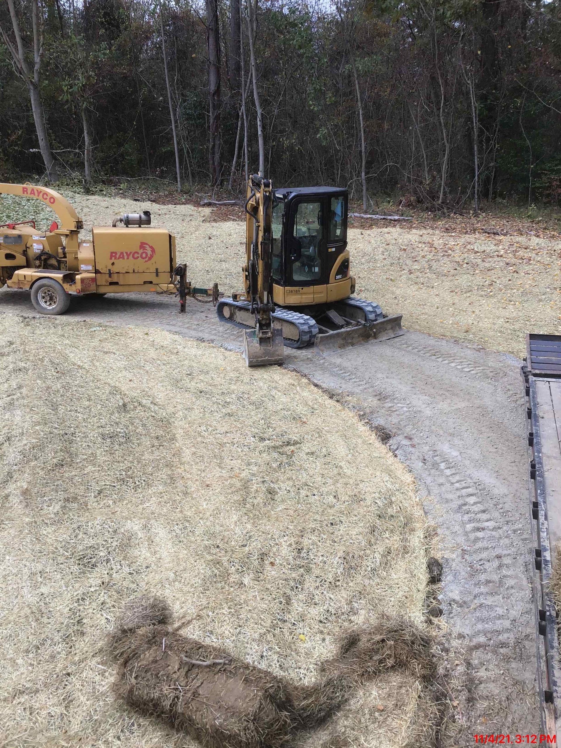A bulldozer is driving down a dirt road next to a pile of hay.