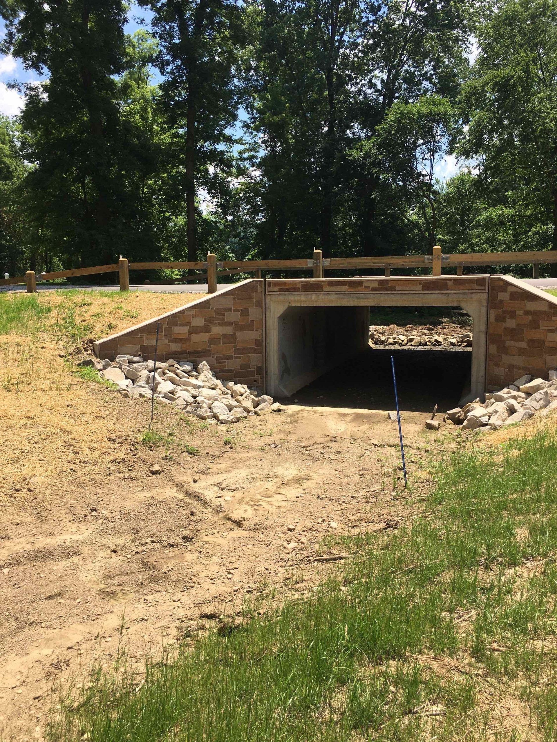 A brick tunnel under a road with a wooden fence in the background.
