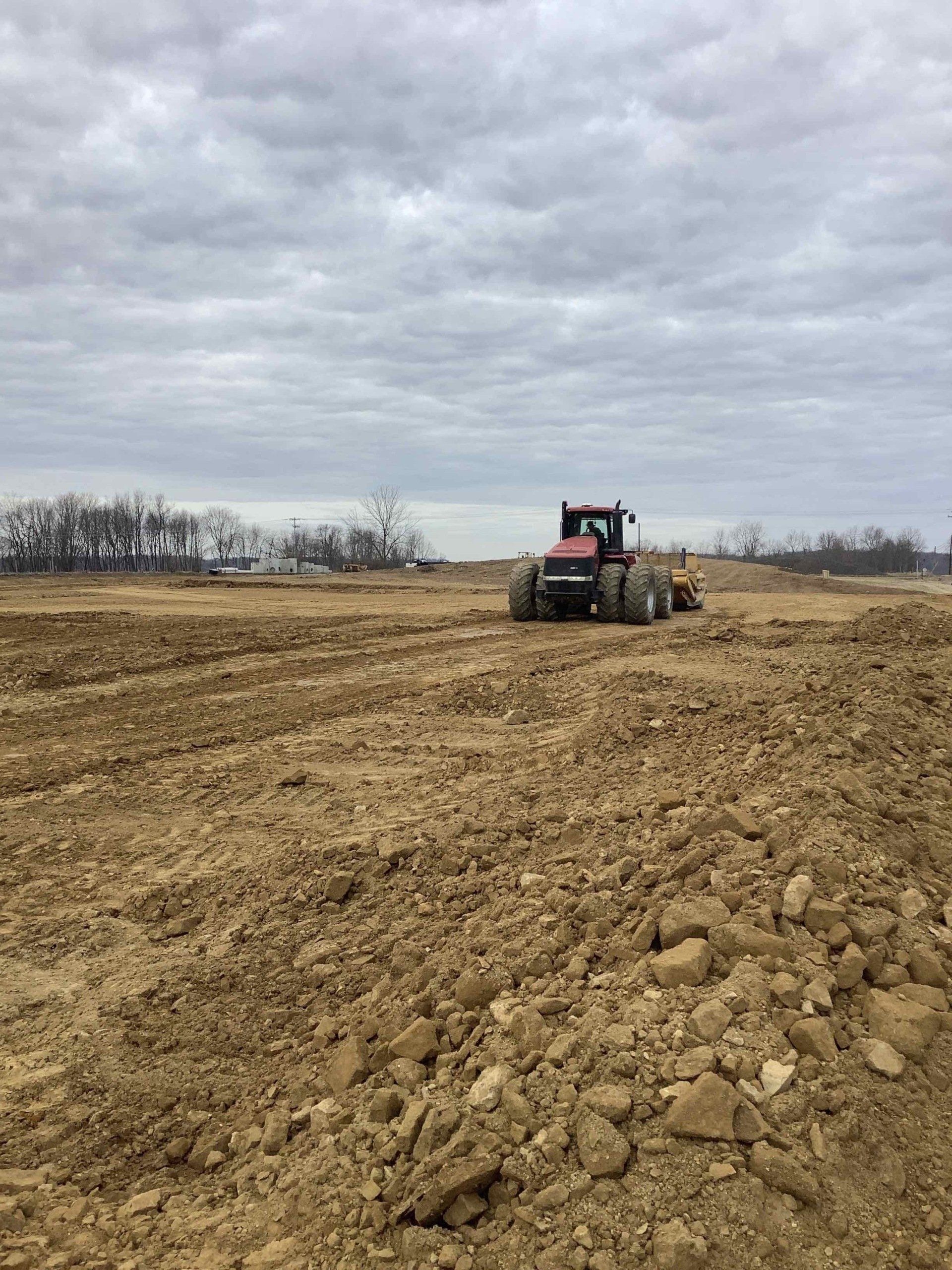 A tractor is plowing a dirt field on a cloudy day.