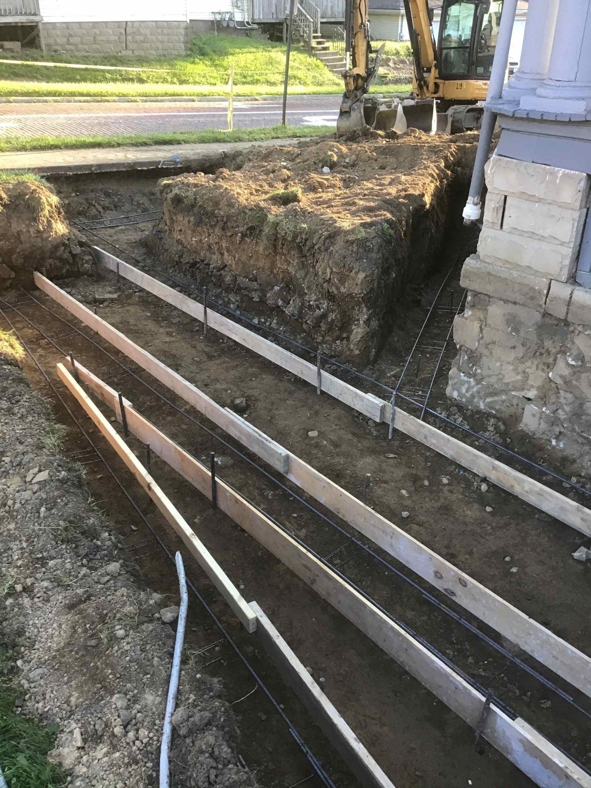 A large excavator is digging a hole in the ground next to a house.