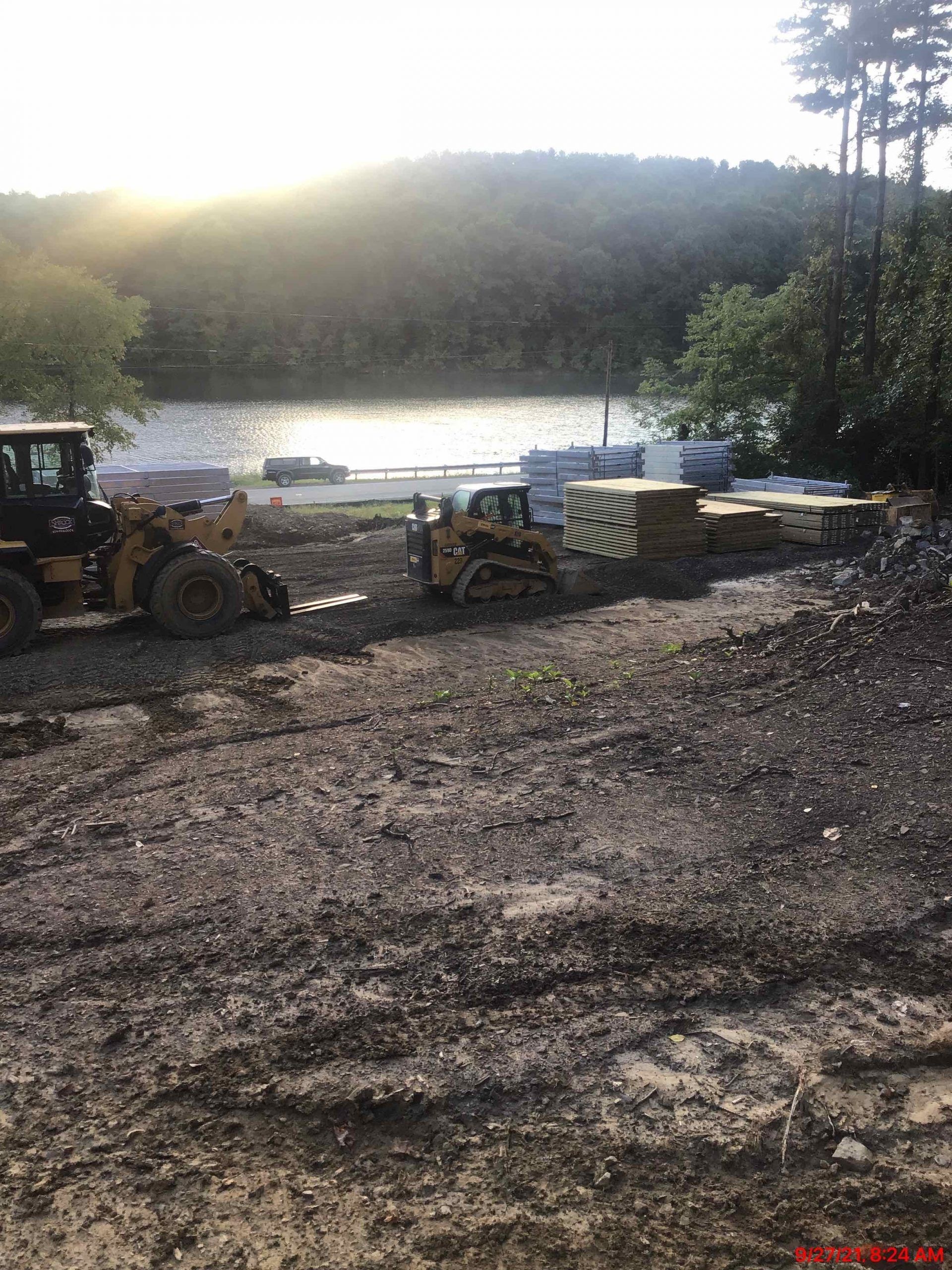 A couple of bulldozers are sitting in a dirt field next to a lake.