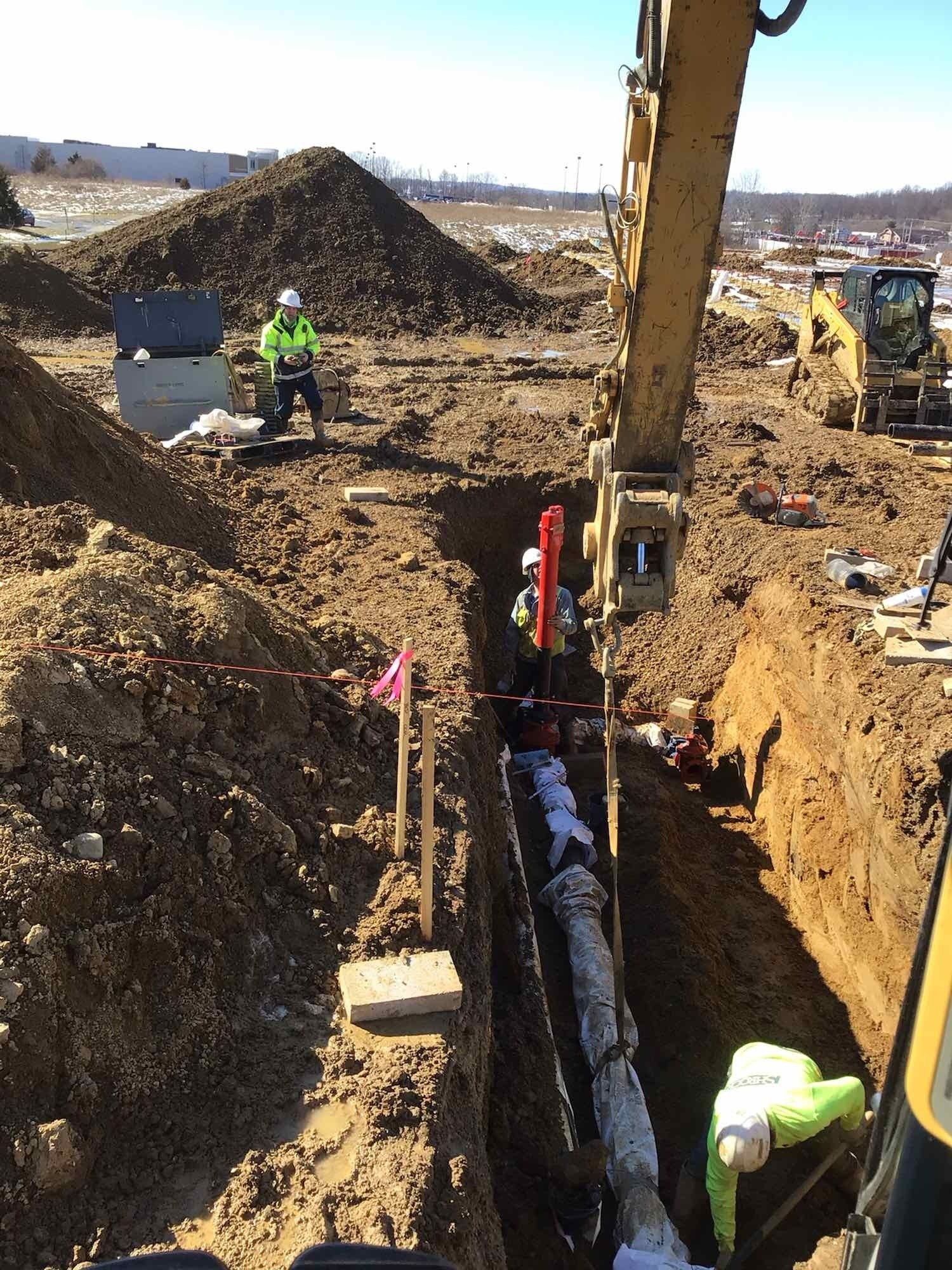 A group of construction workers are working on a pipe in the dirt.