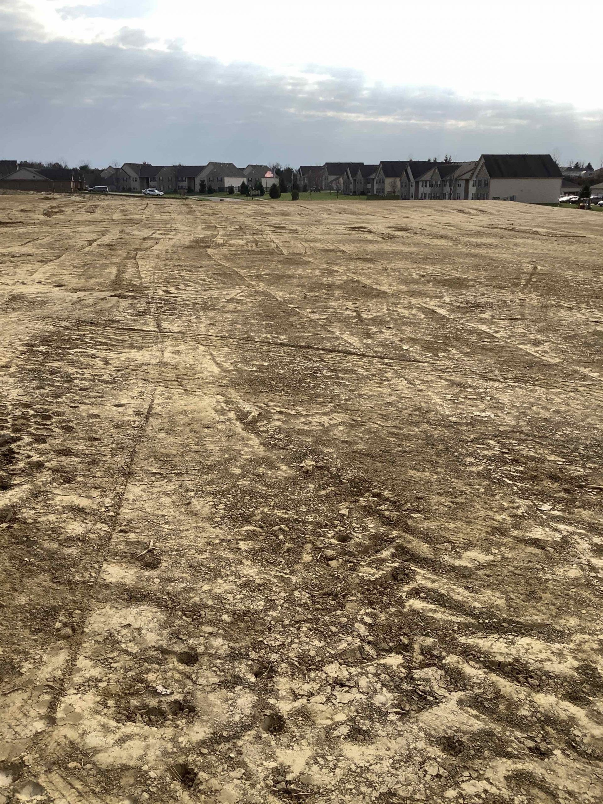 A large dirt field with houses in the background.