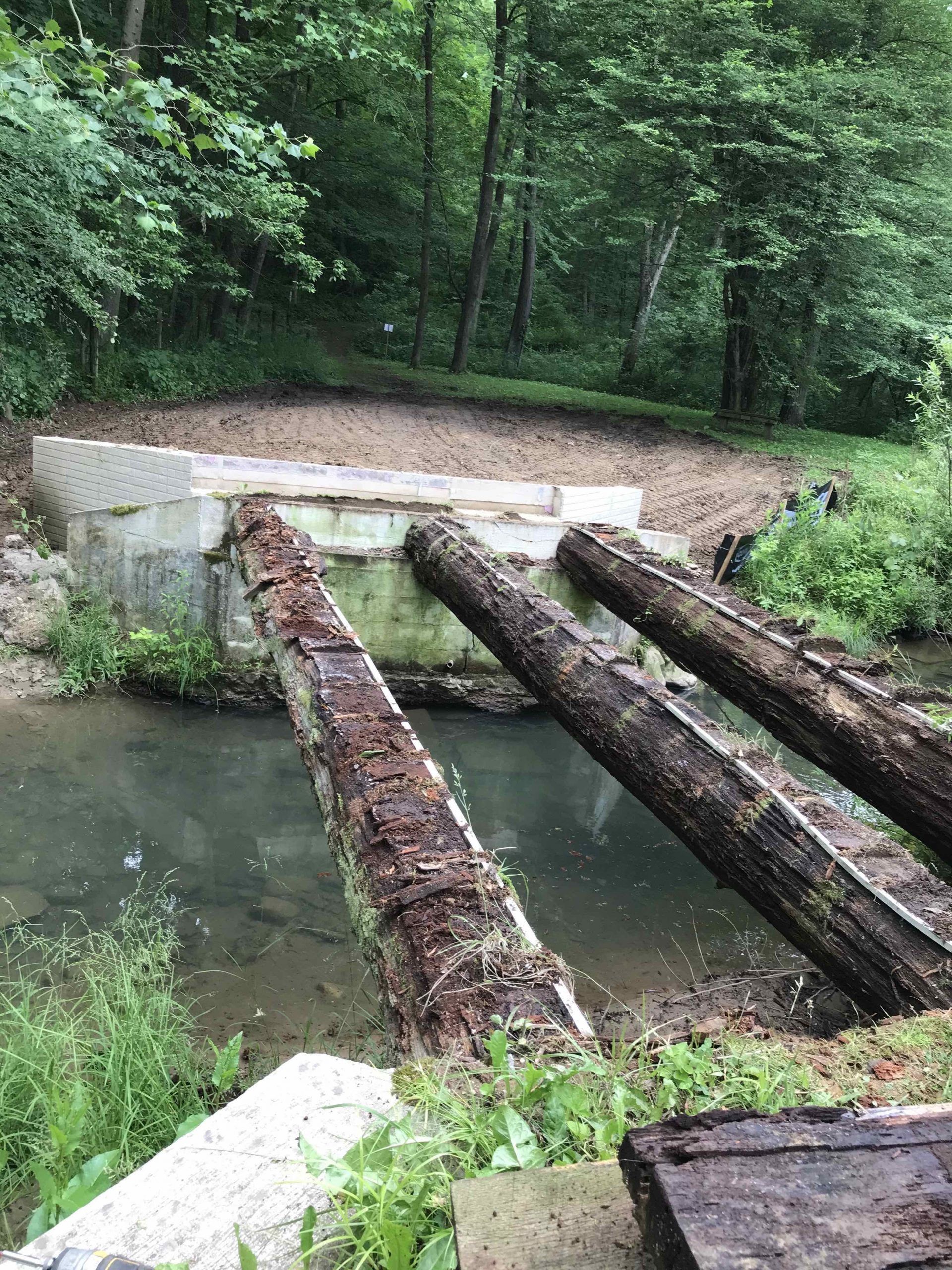 A bridge made of logs over a river in the woods.