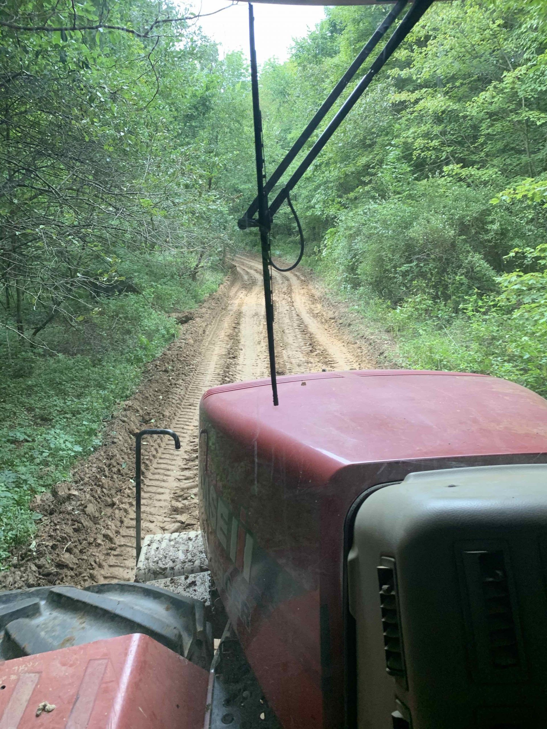 A red tractor is driving down a dirt road in the woods.