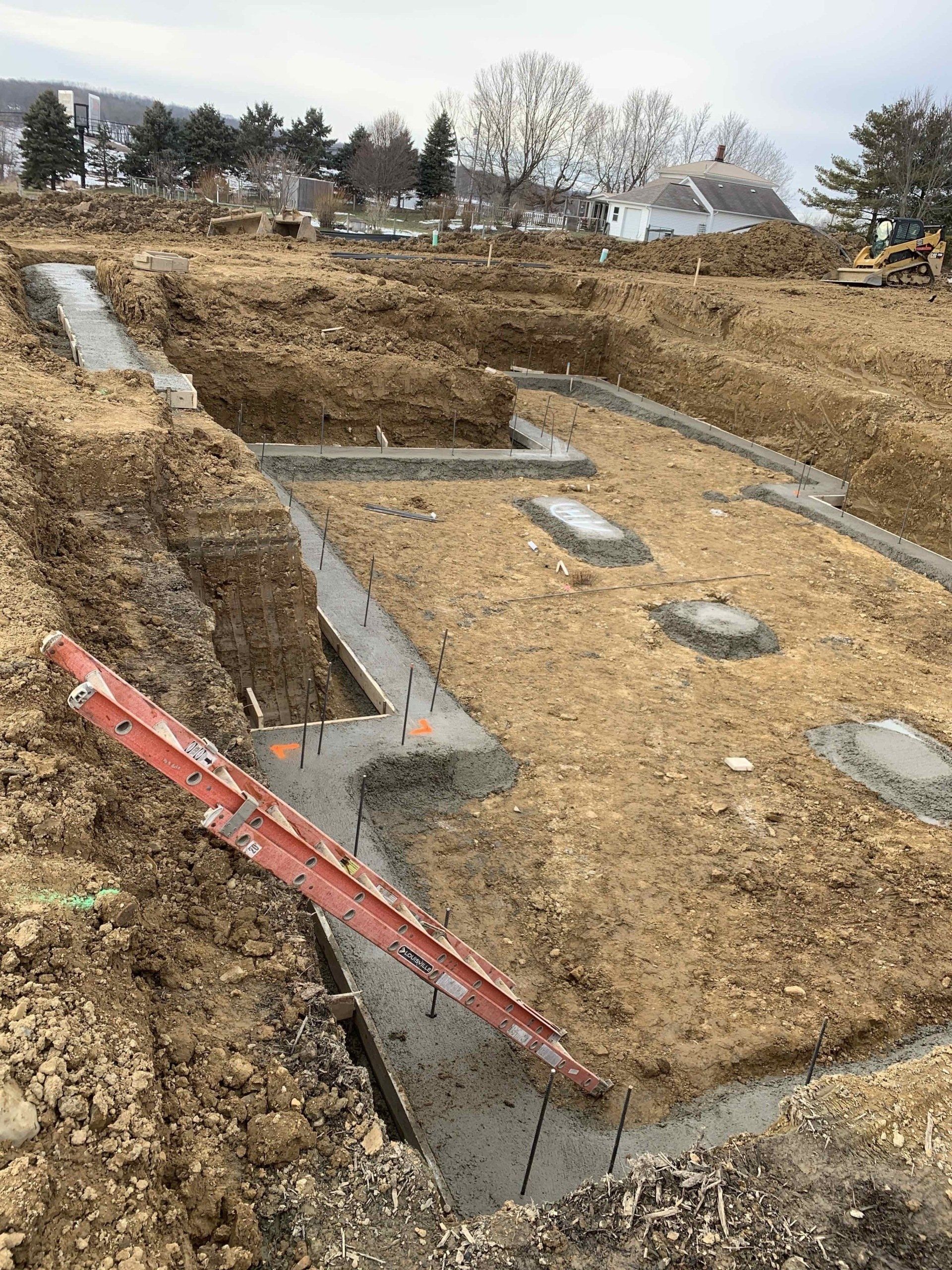 A construction site with a red ladder in the dirt.