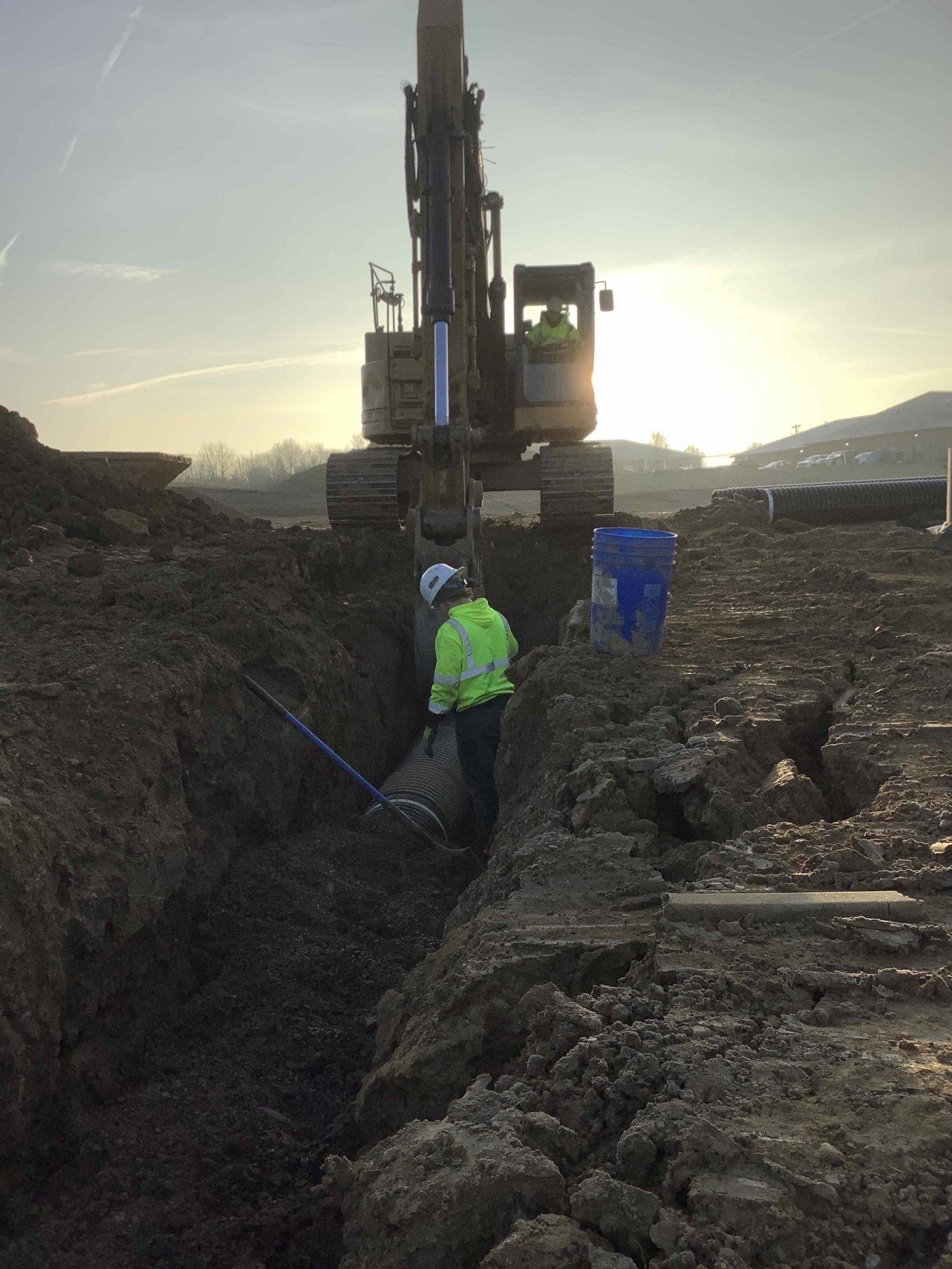 A man is standing in the dirt next to a large excavator.