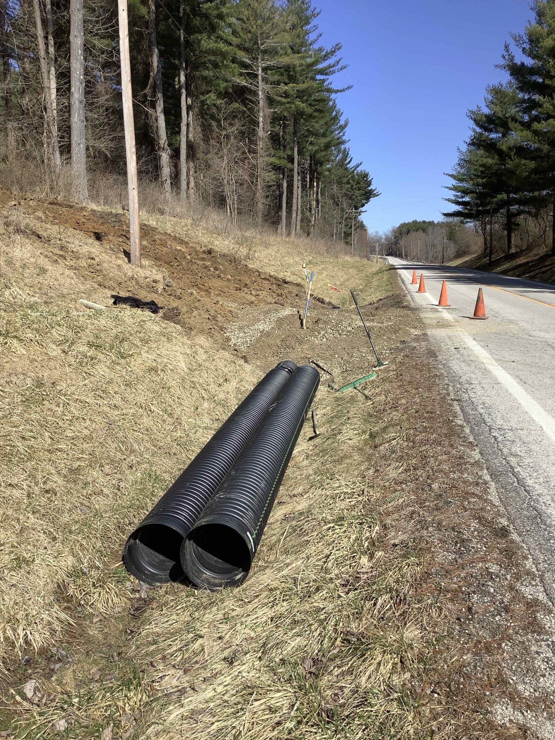 A large black pipe is laying on the side of a road next to a forest.