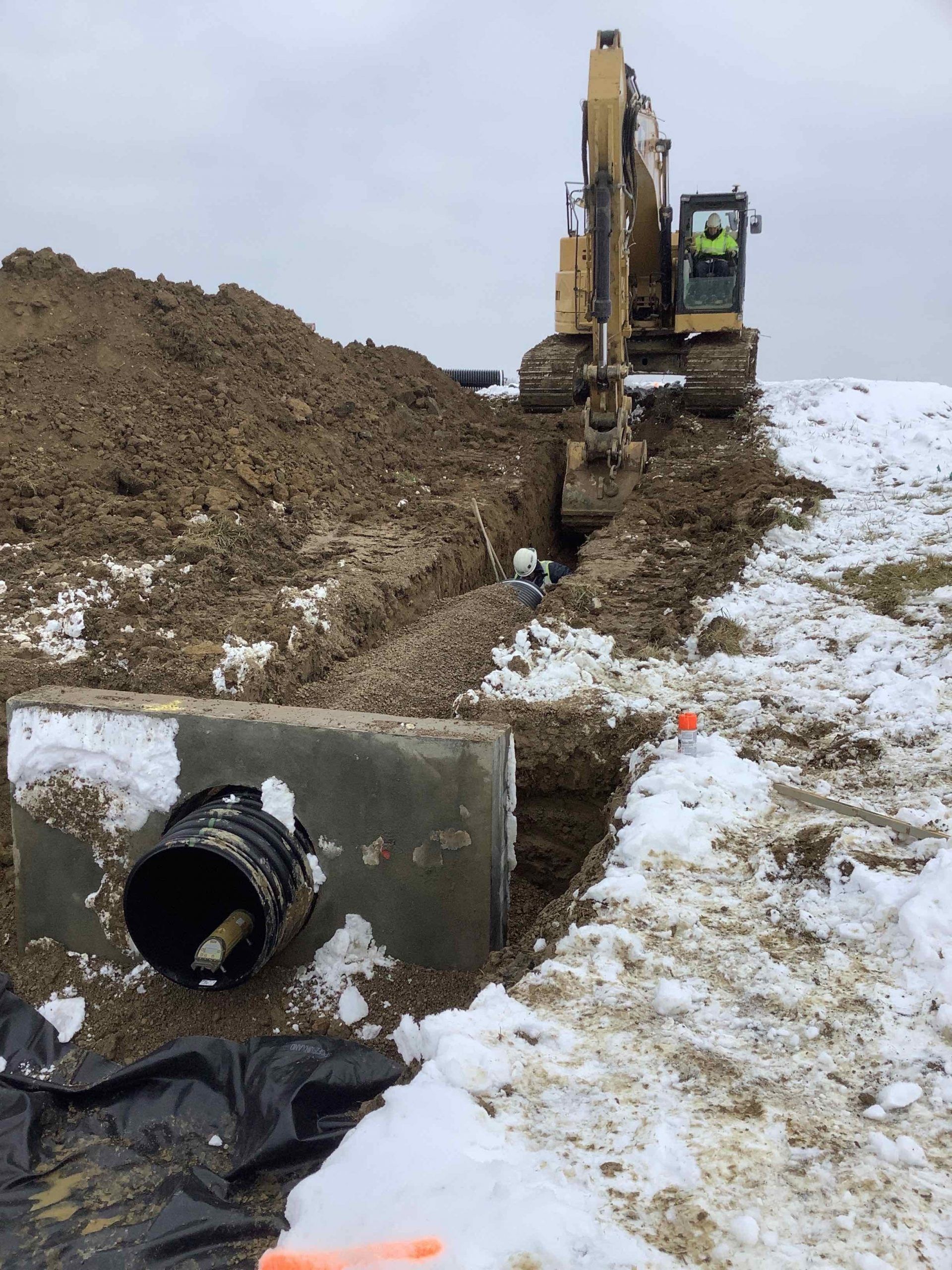 A large excavator is digging a hole in the ground in the snow.
