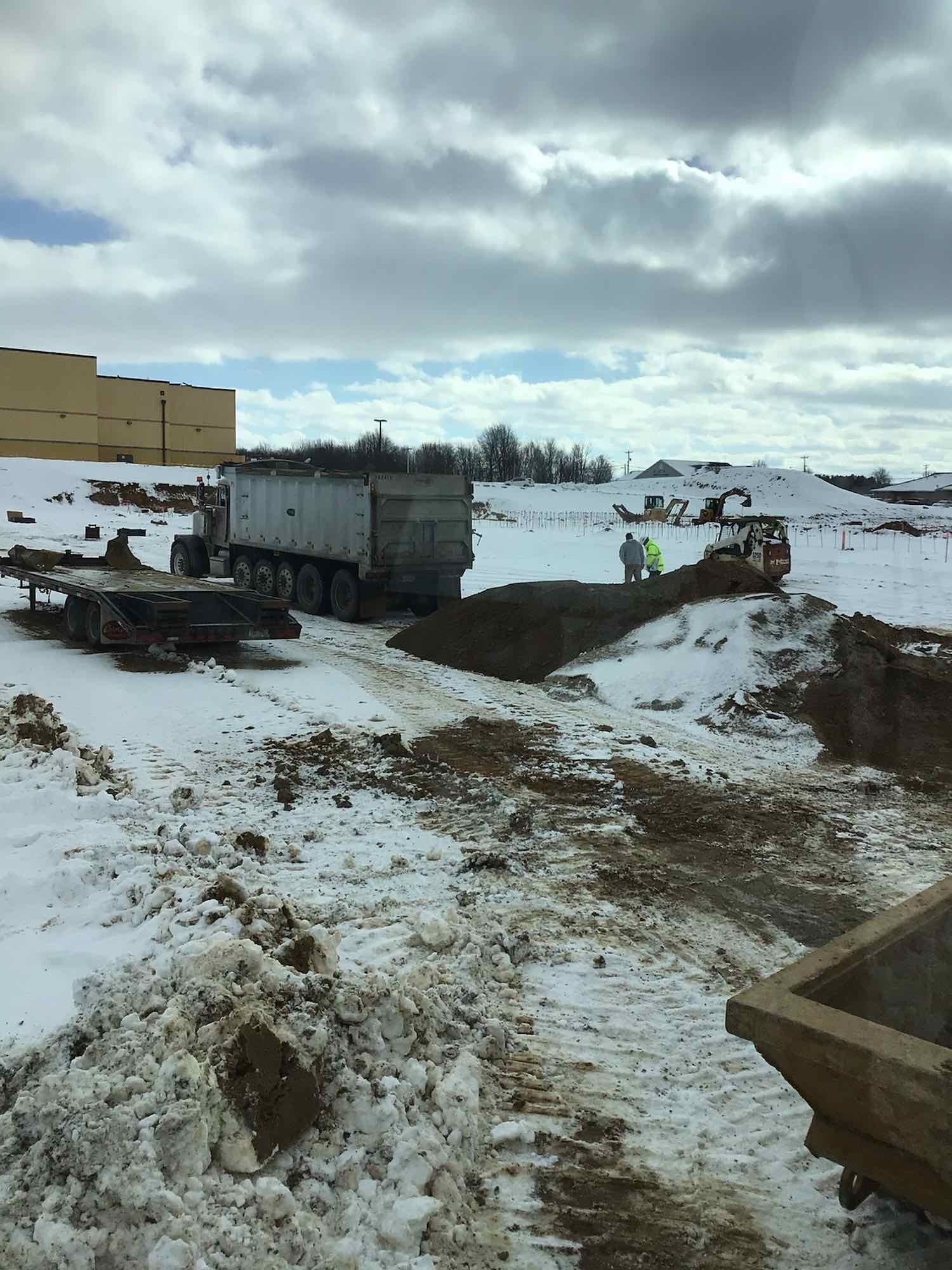A dump truck is parked in the snow on a construction site.