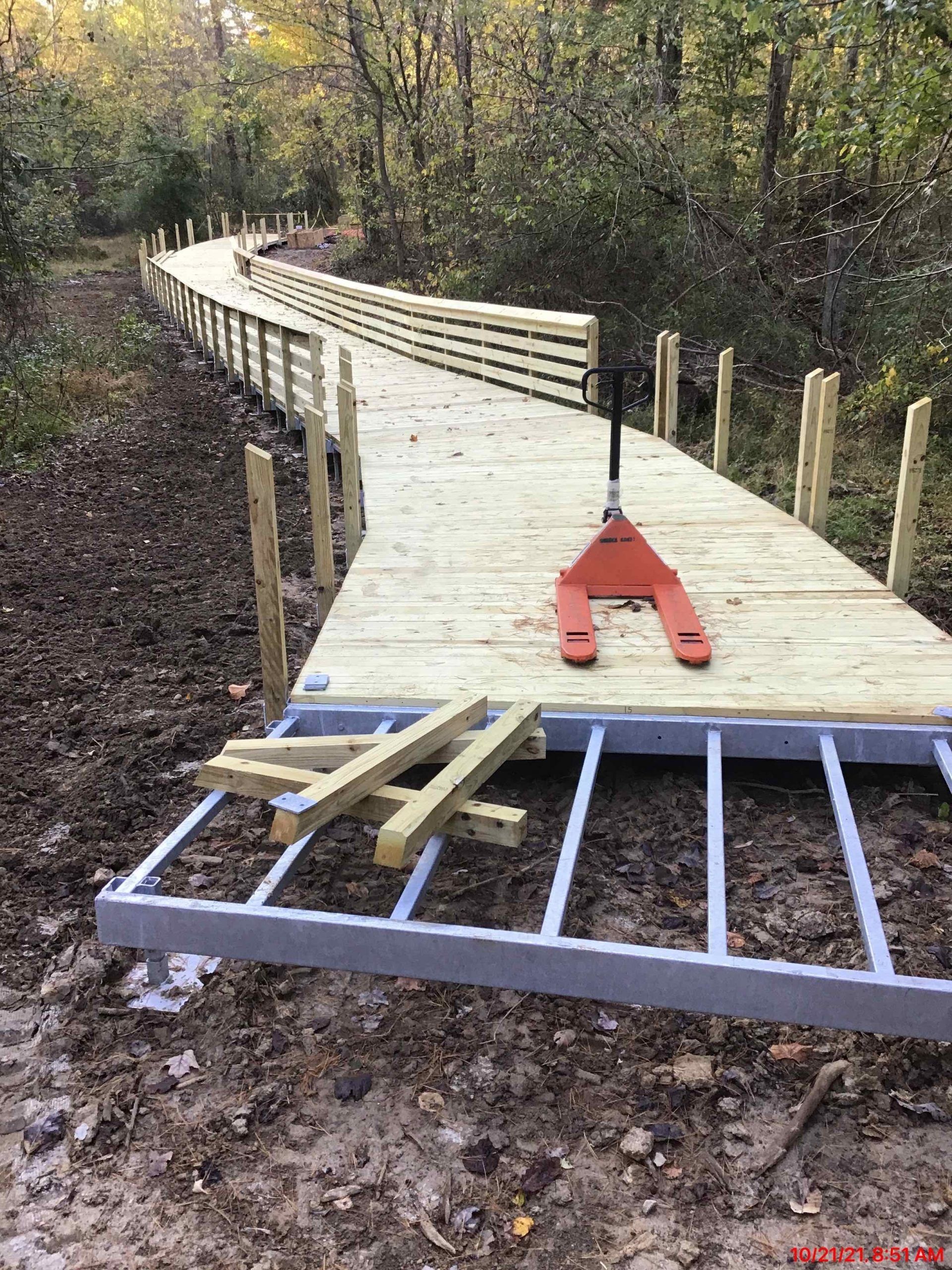A wooden walkway is being built in the woods with a pallet jack.