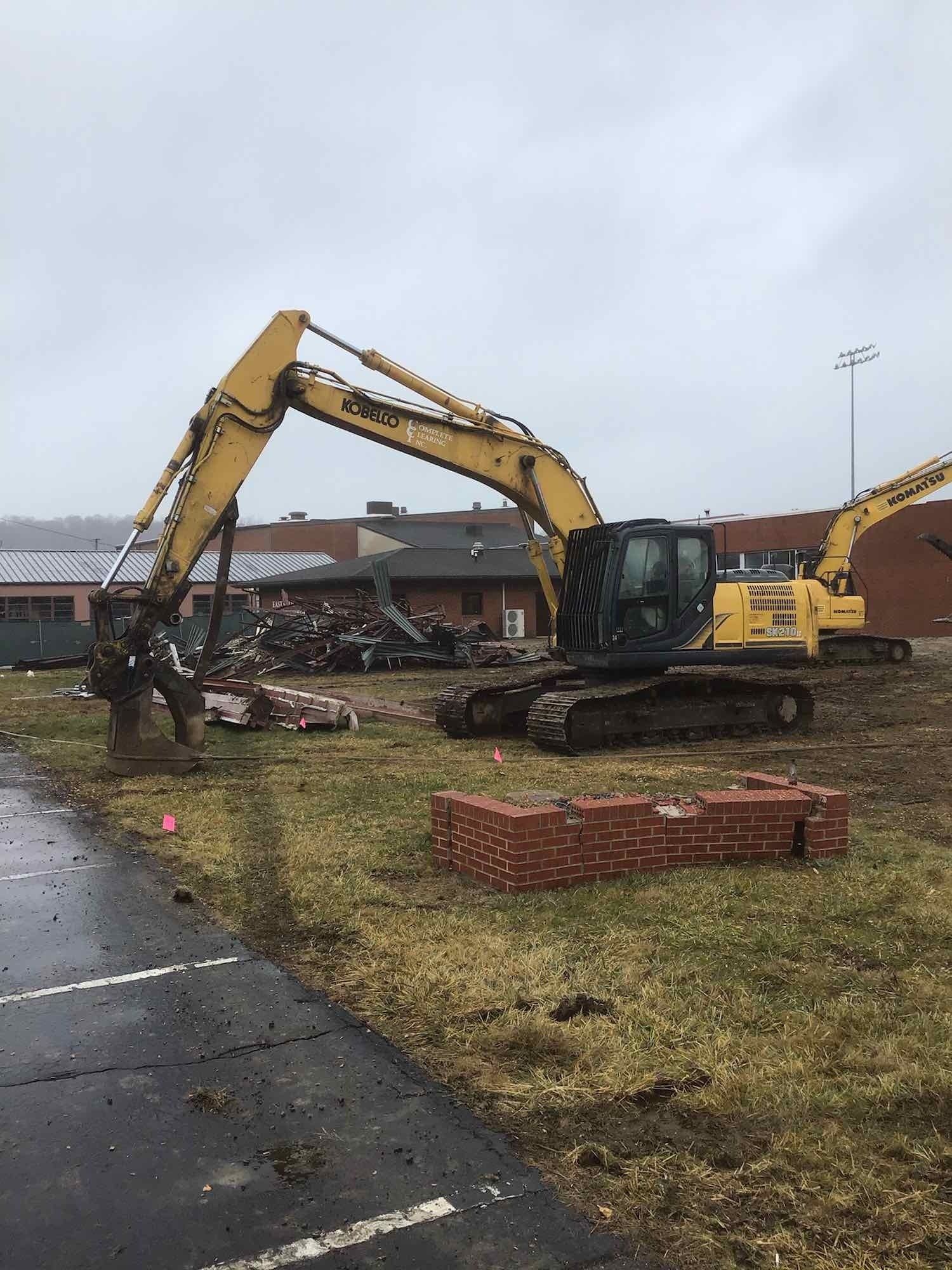 A large yellow excavator is sitting in a field next to a road.