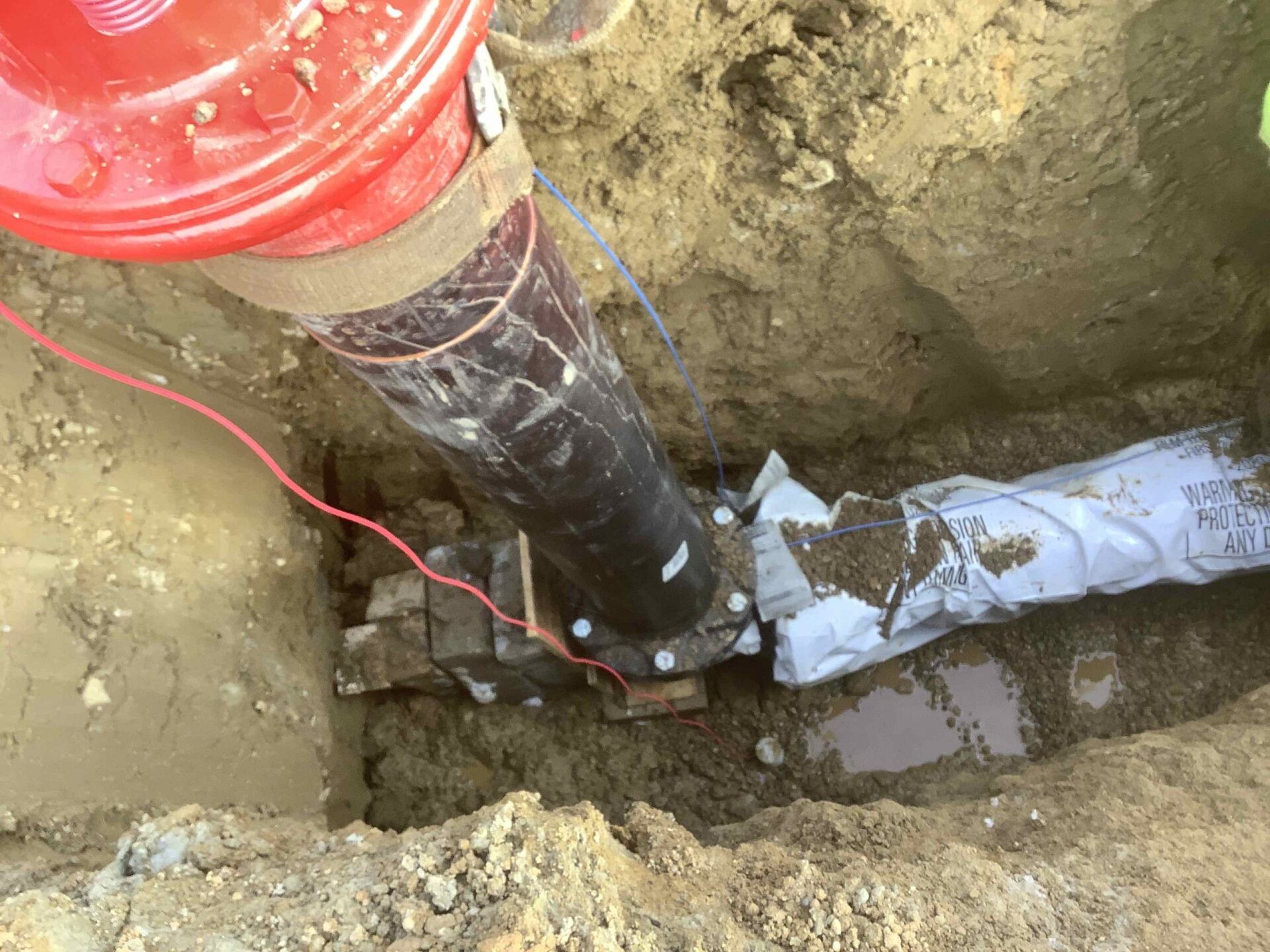 A red fire hydrant is sitting in the dirt next to a black pipe.