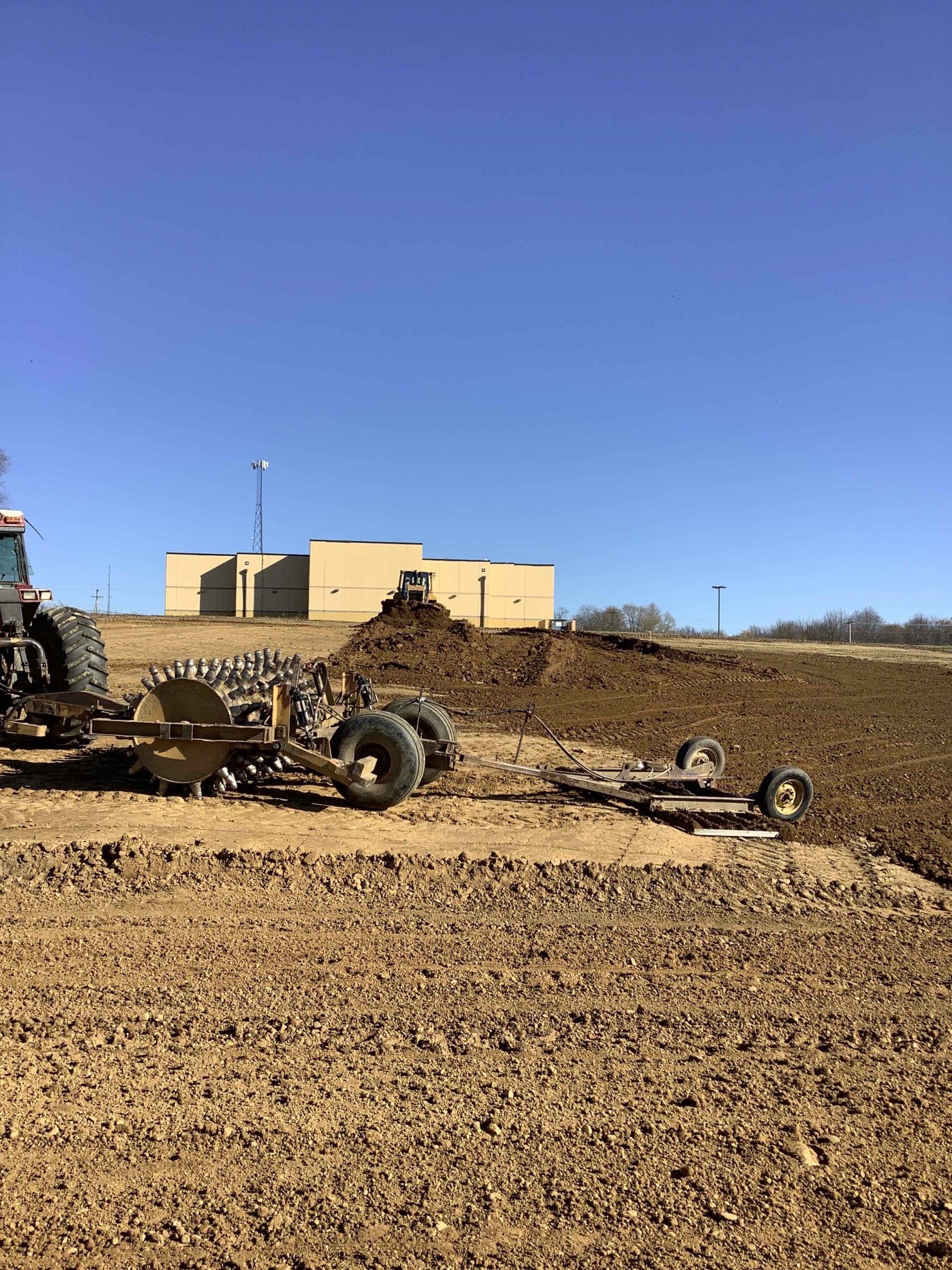 A tractor is plowing a field with a building in the background.