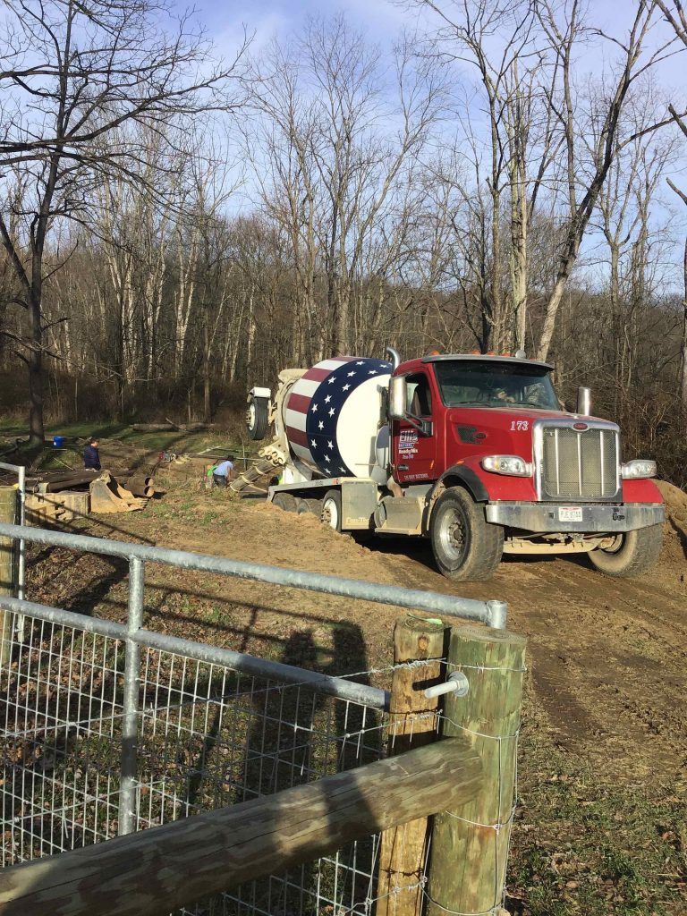 A red and white truck with an american flag on the back is parked in a dirt field.