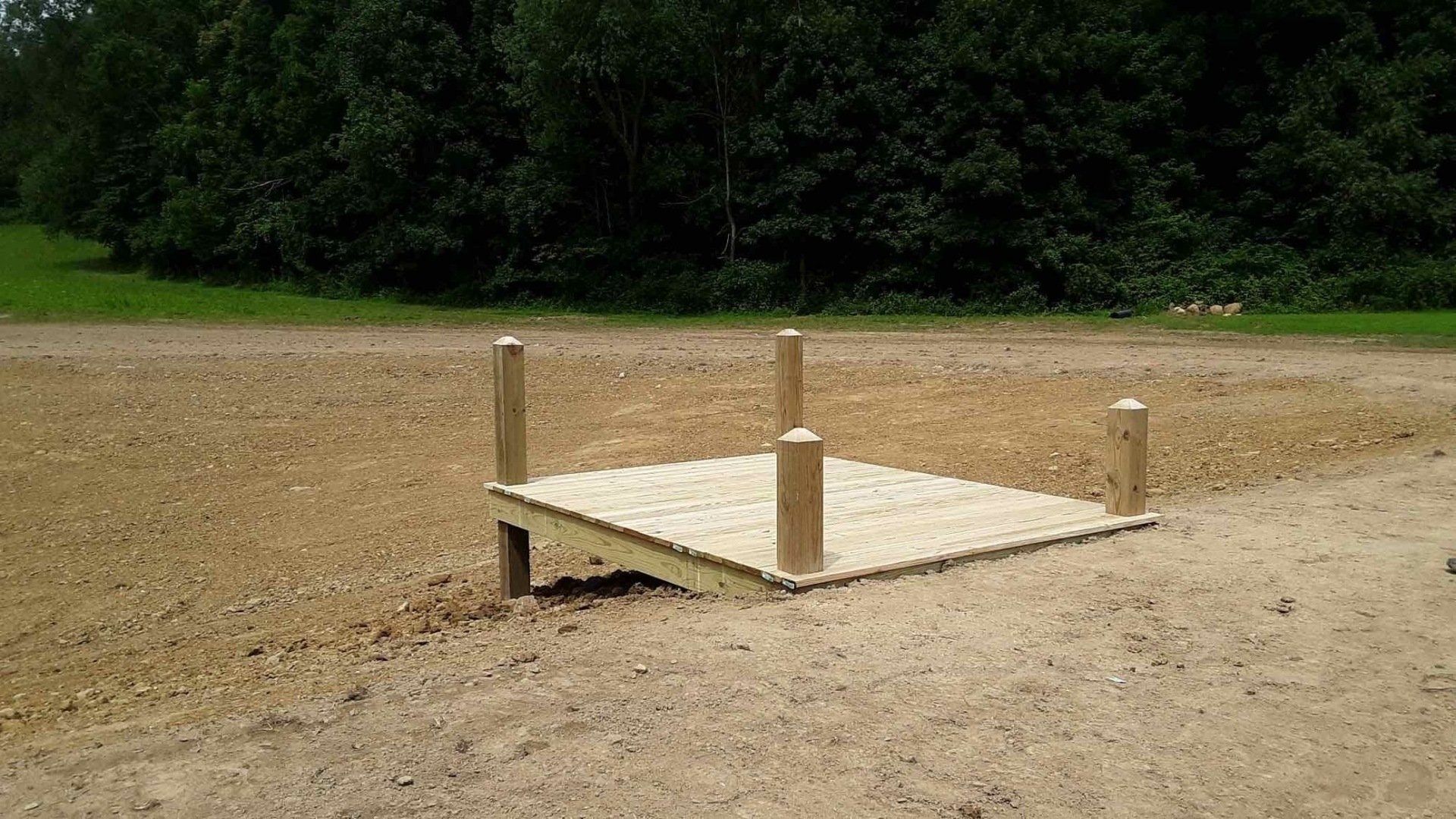 A wooden platform is sitting in the middle of a dirt field.