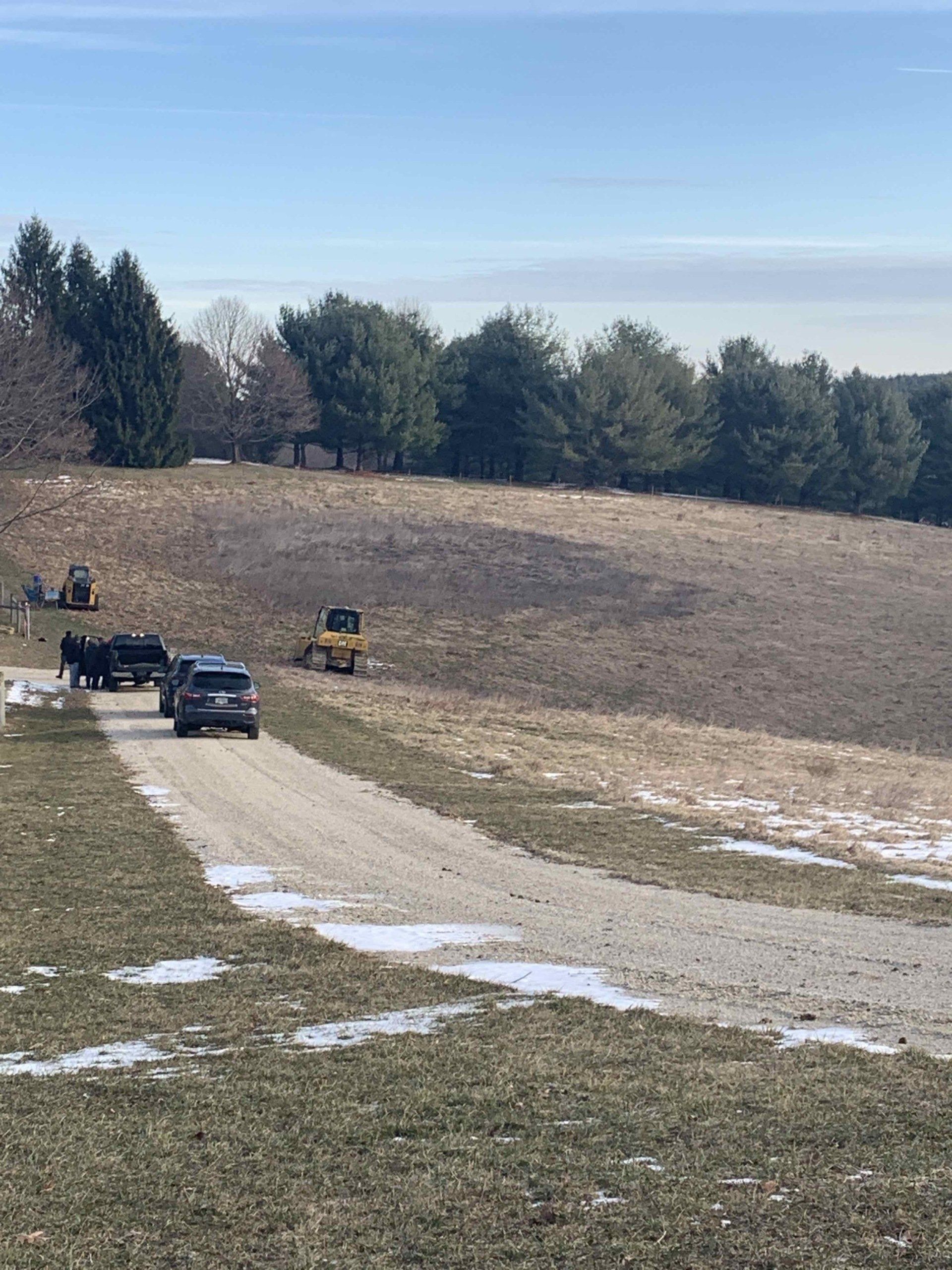 A group of cars are driving down a dirt road in a field.