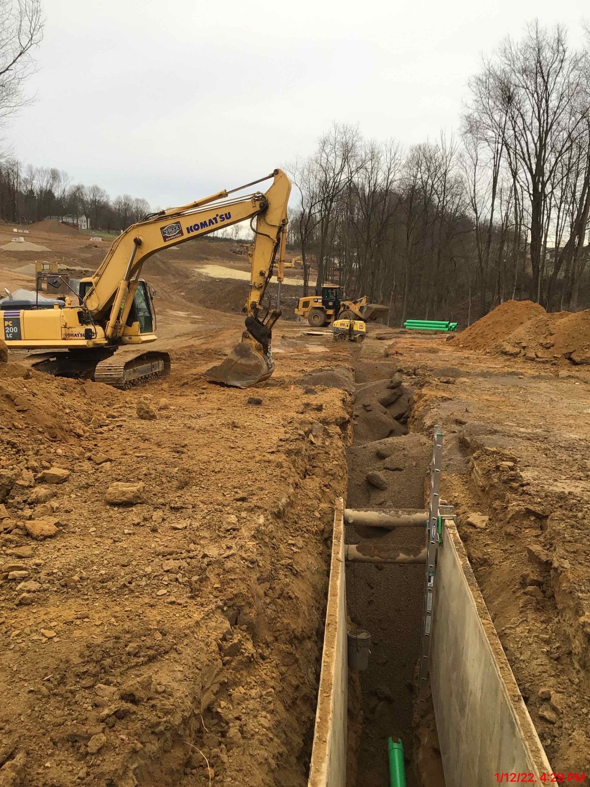 A yellow excavator is digging a trench in the dirt.