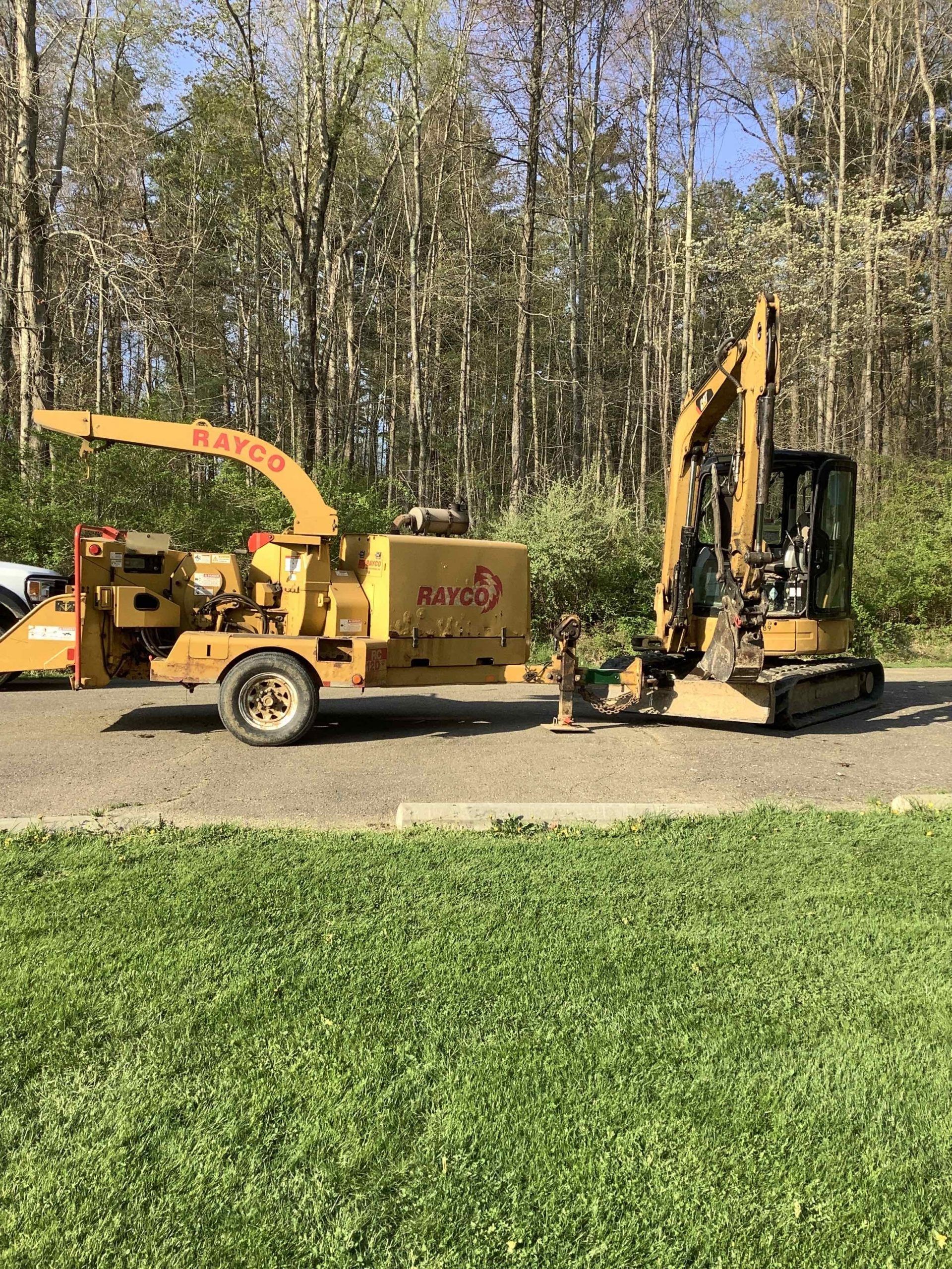 A tree chipper and an excavator are parked next to each other on a dirt road.