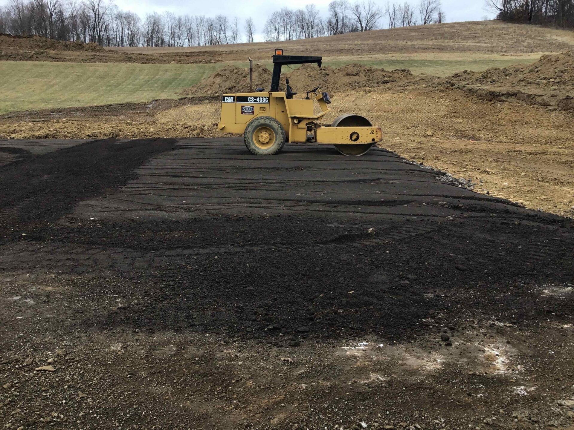A yellow roller is sitting on top of a pile of dirt in a field.