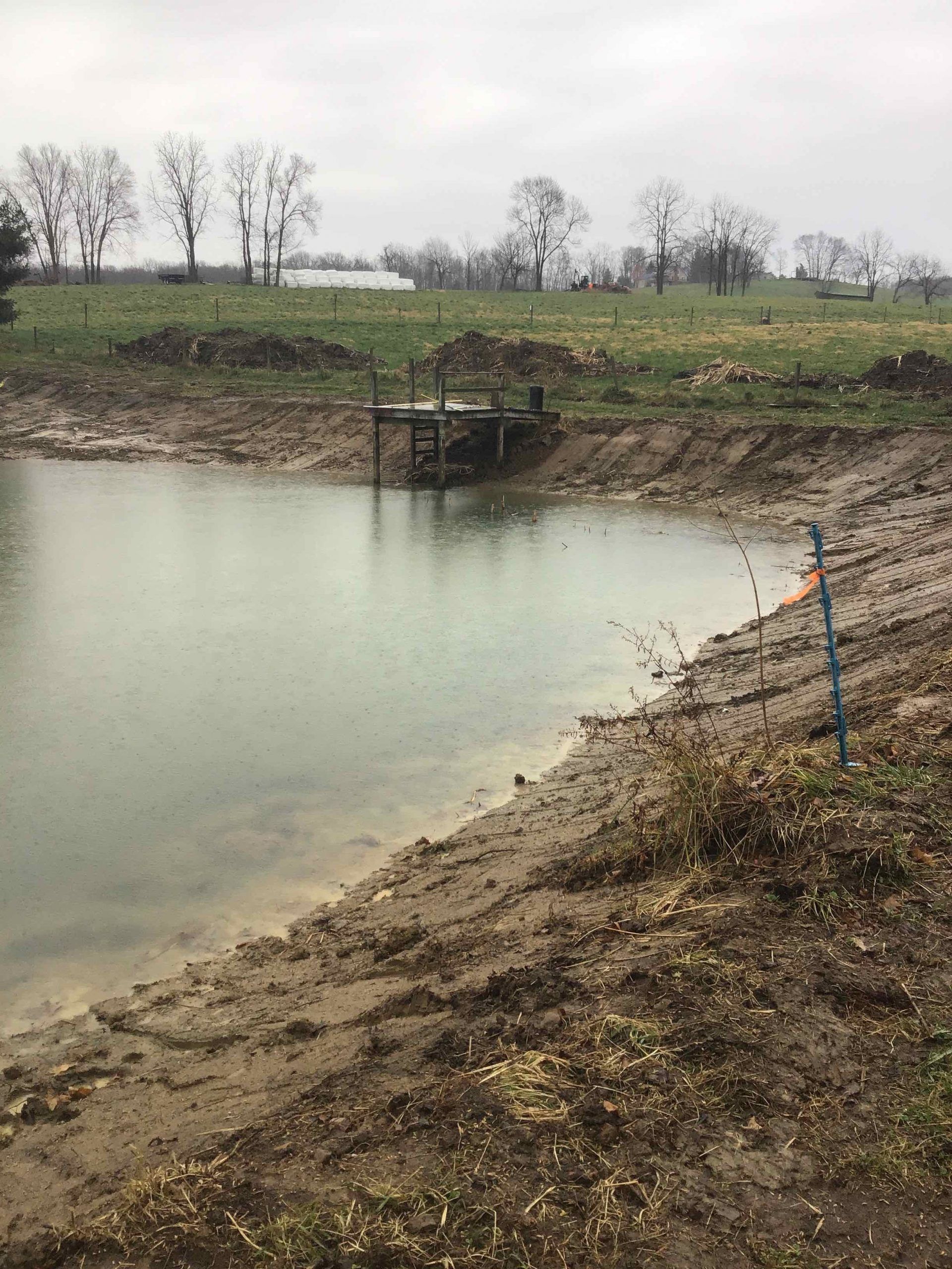 A small pond in the middle of a field with a fence around it.