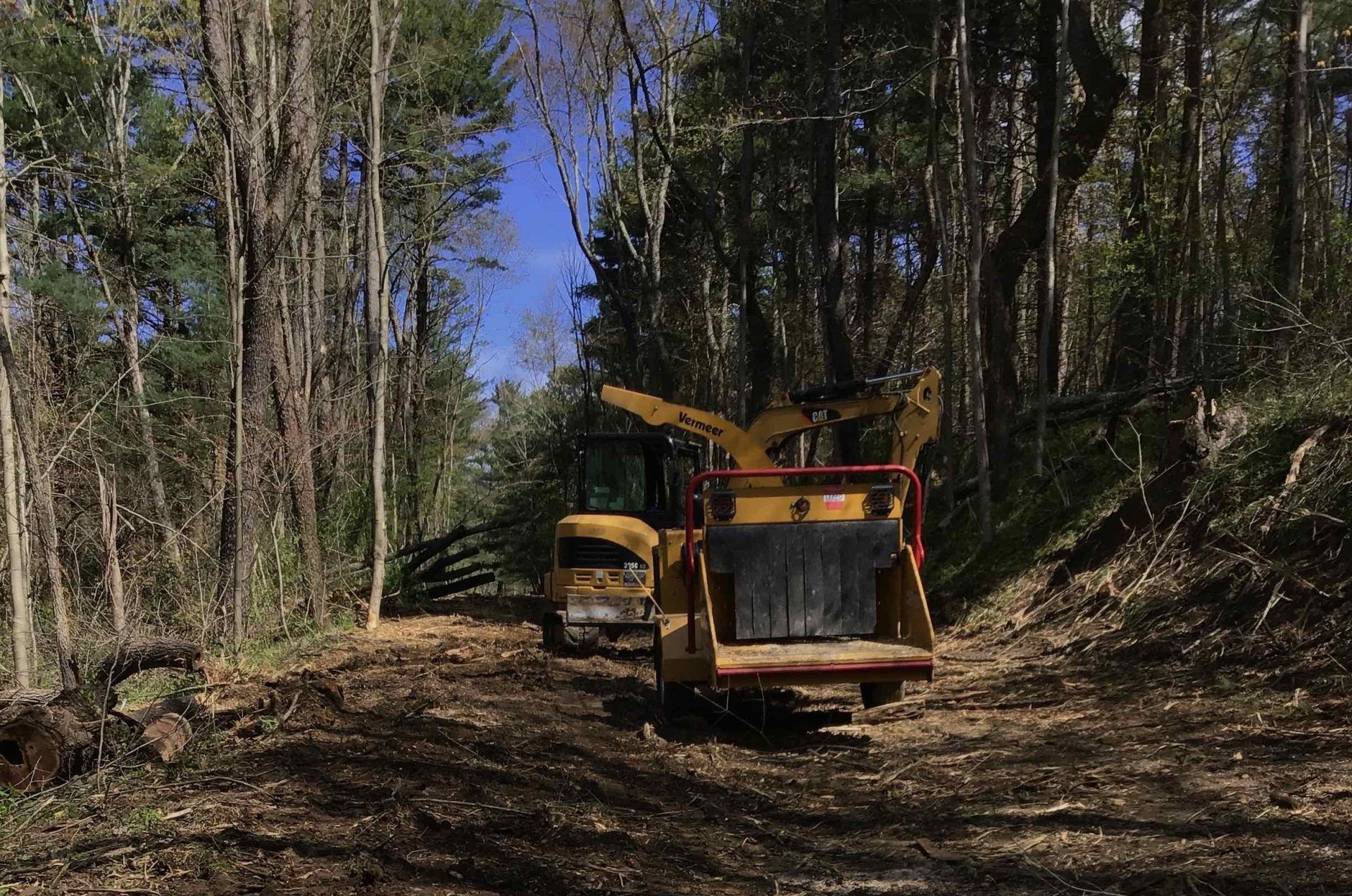 A yellow truck is driving down a dirt road in the woods.