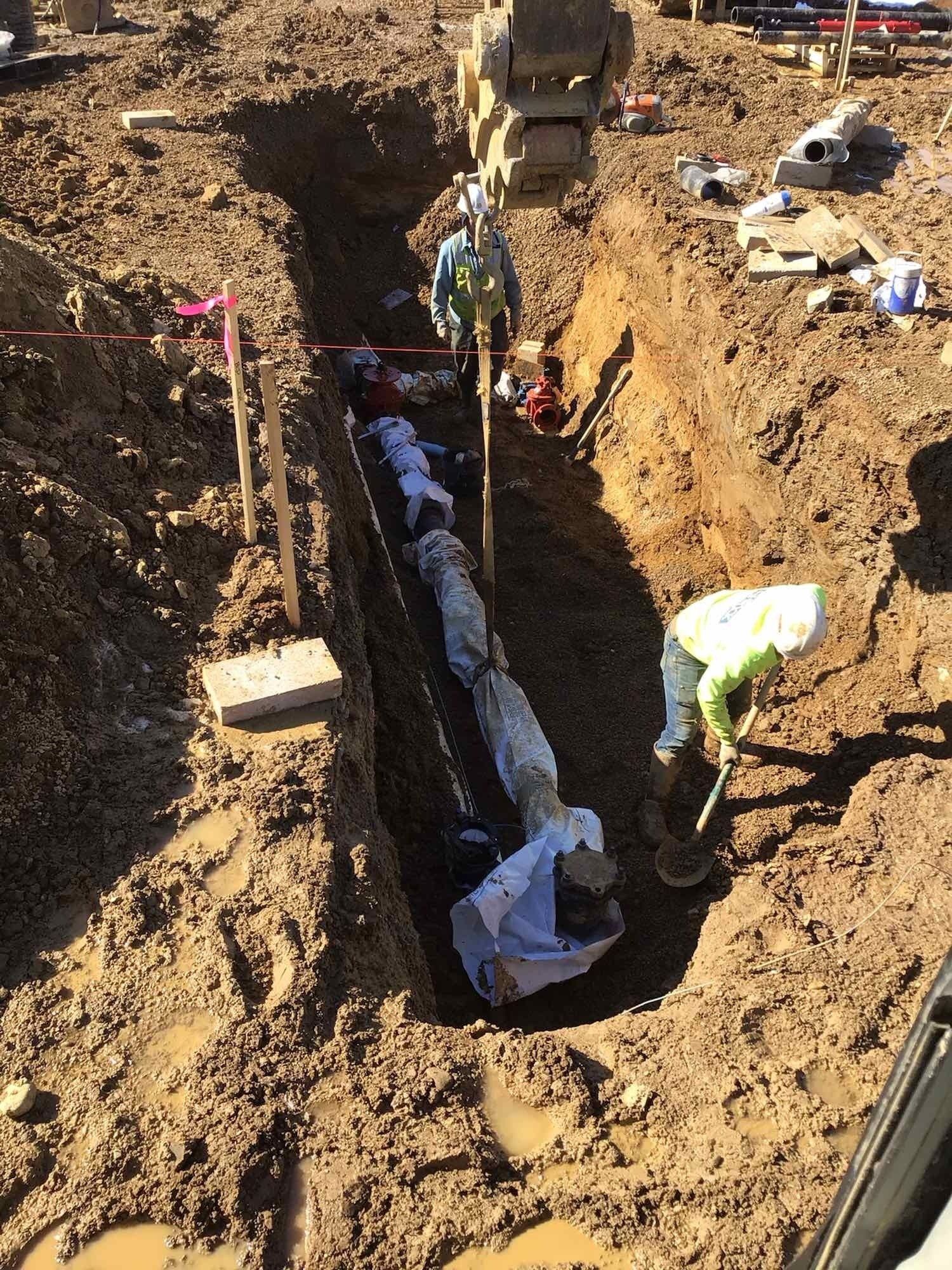 A group of people are working on a pipe in the dirt.