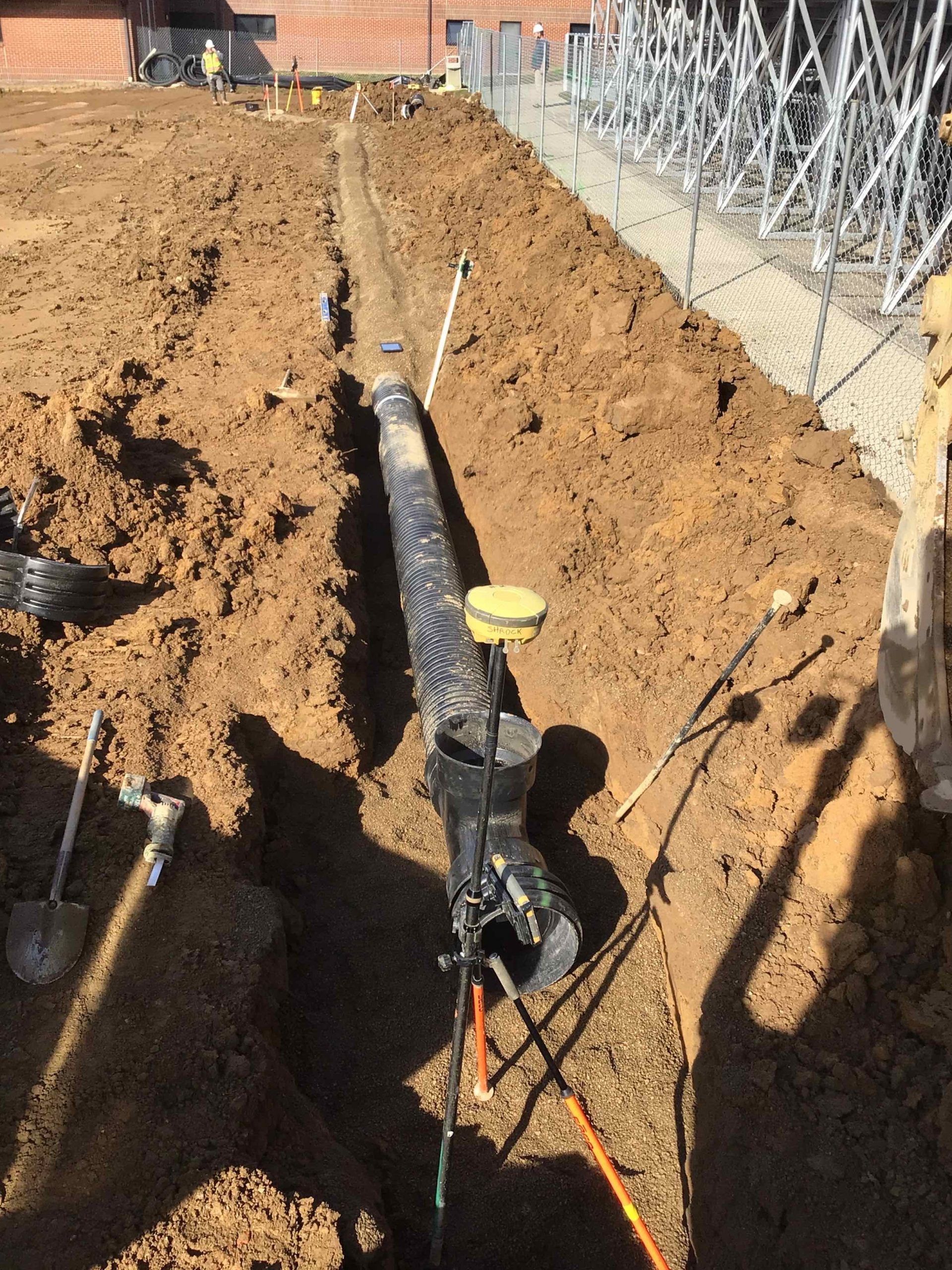 A pipe is being installed in the dirt next to a fence.