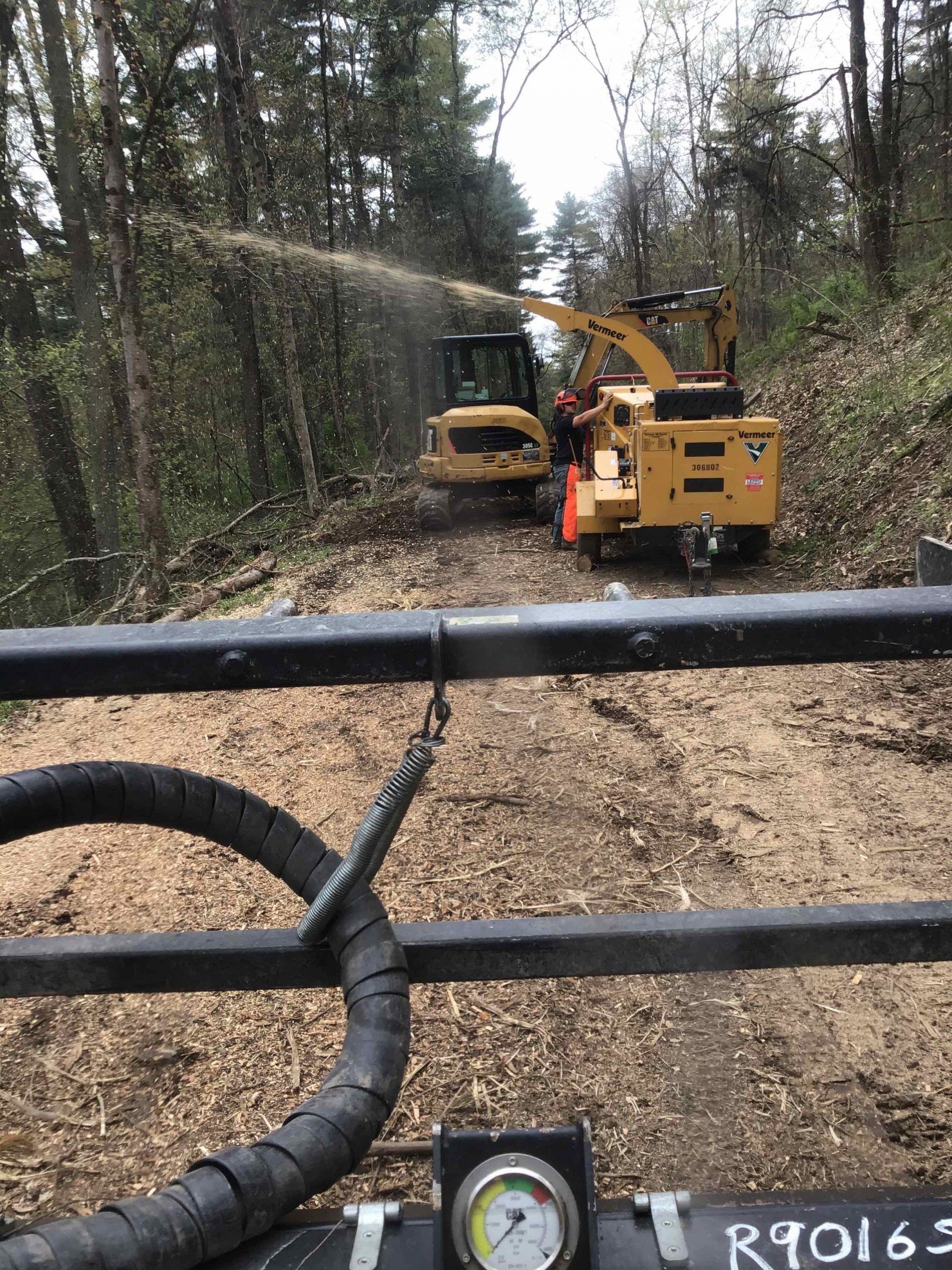 A couple of tractors are driving down a dirt road in the woods.