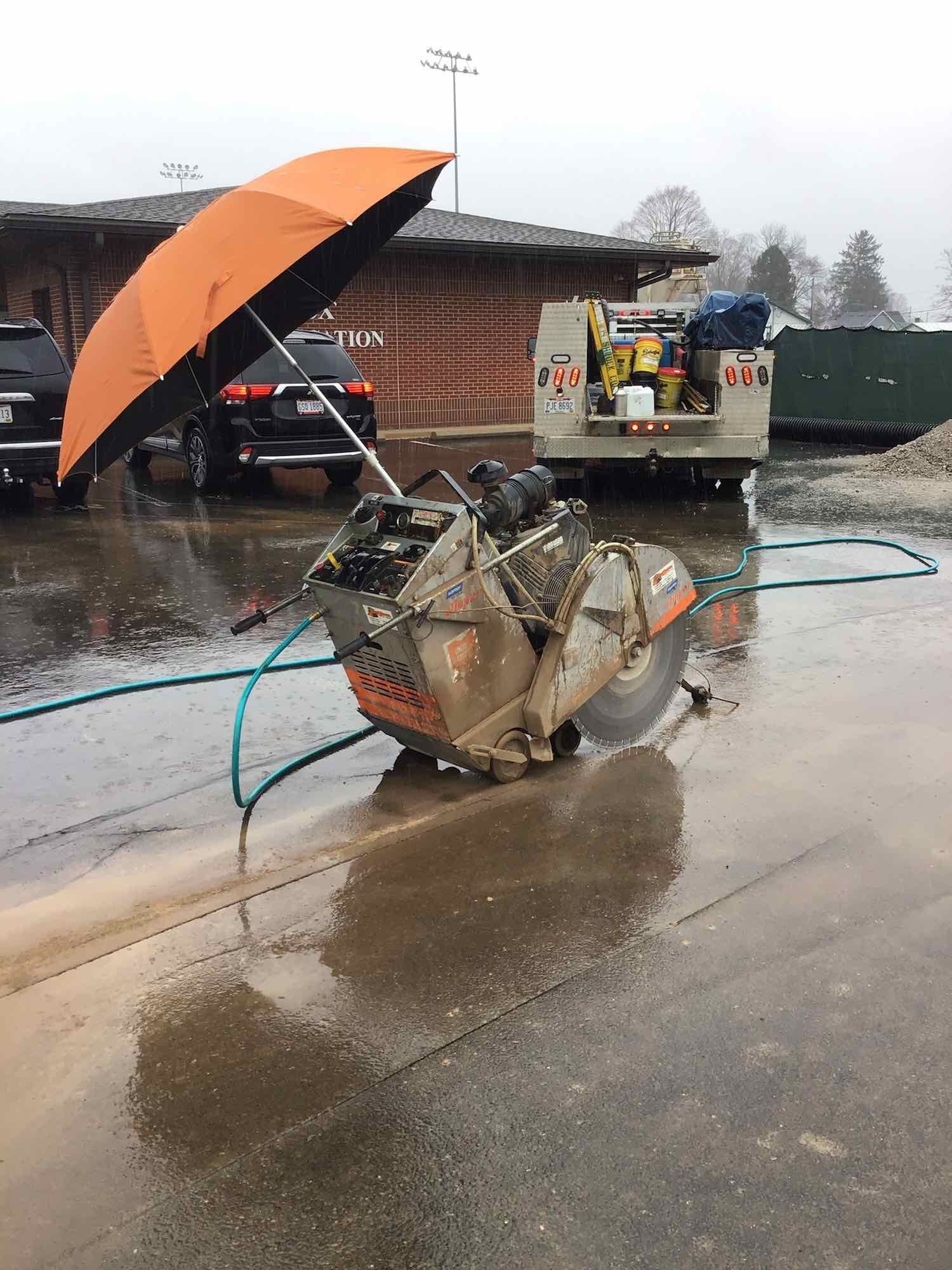 A concrete saw is sitting on the side of the road next to an umbrella.