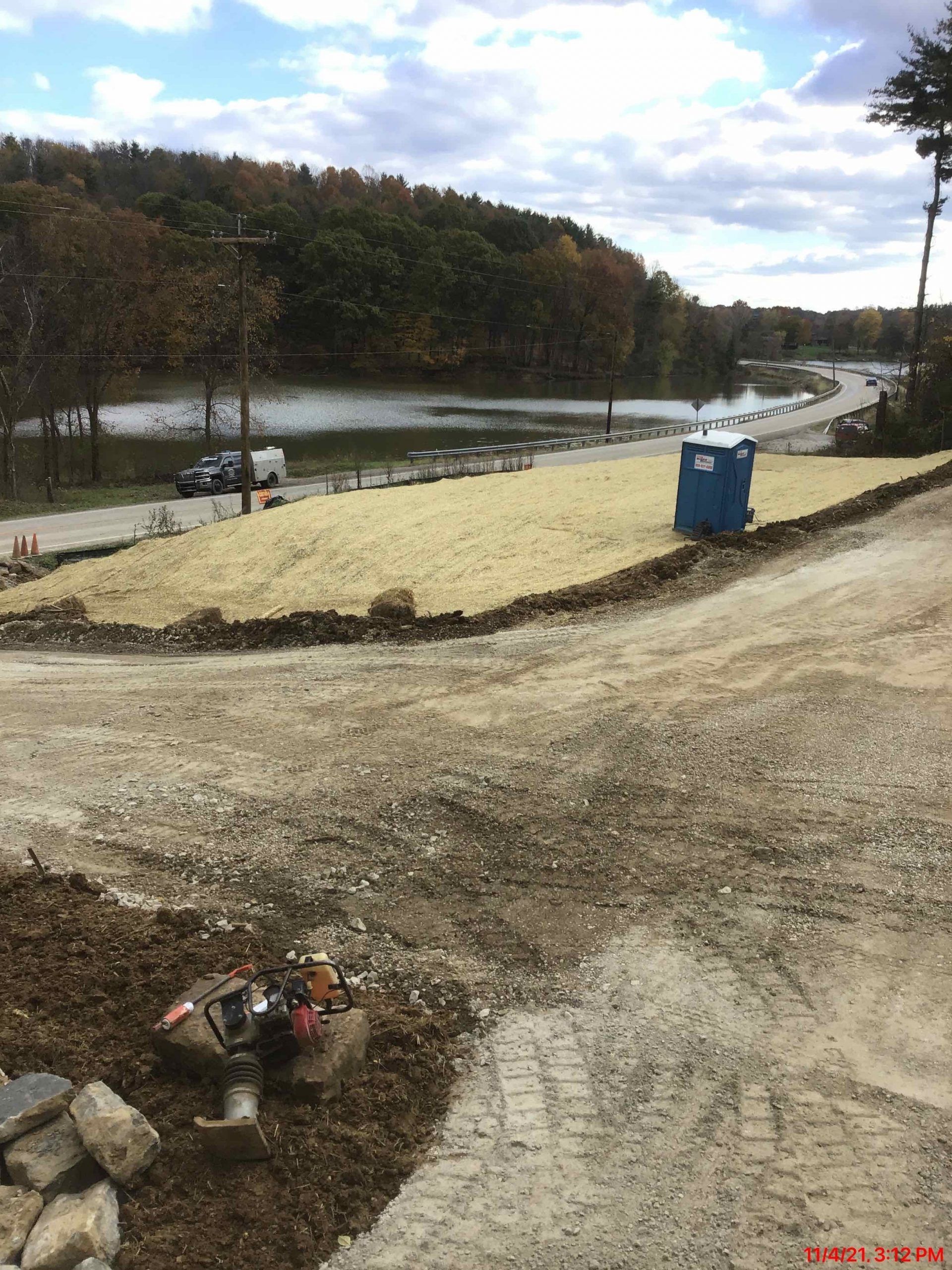 A blue portable toilet is sitting on the side of a dirt road.