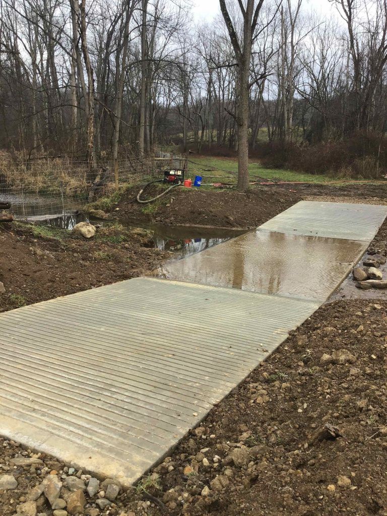 A concrete walkway is being built next to a river in the woods.