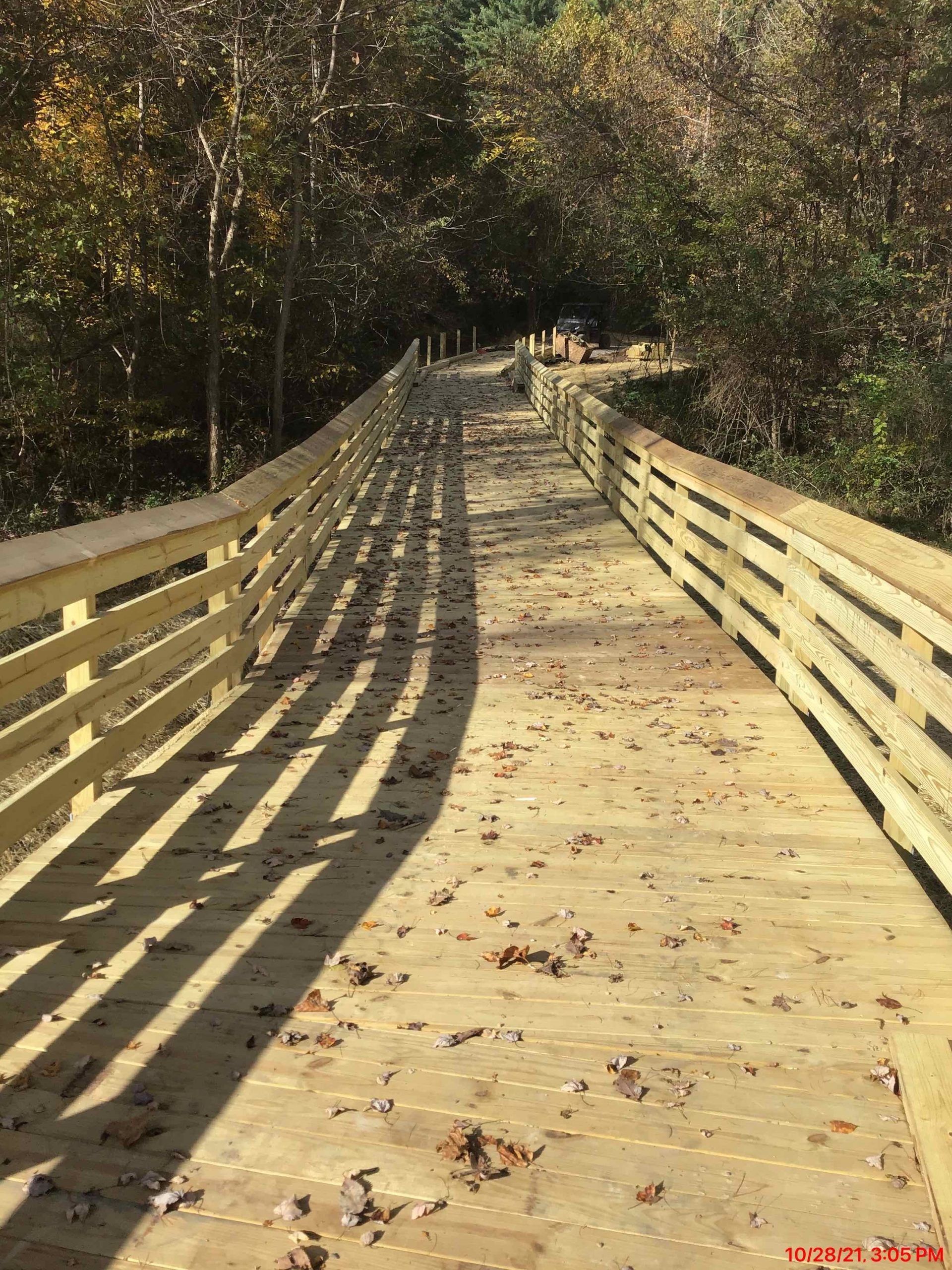 A wooden bridge in the middle of a forest with leaves on the ground.