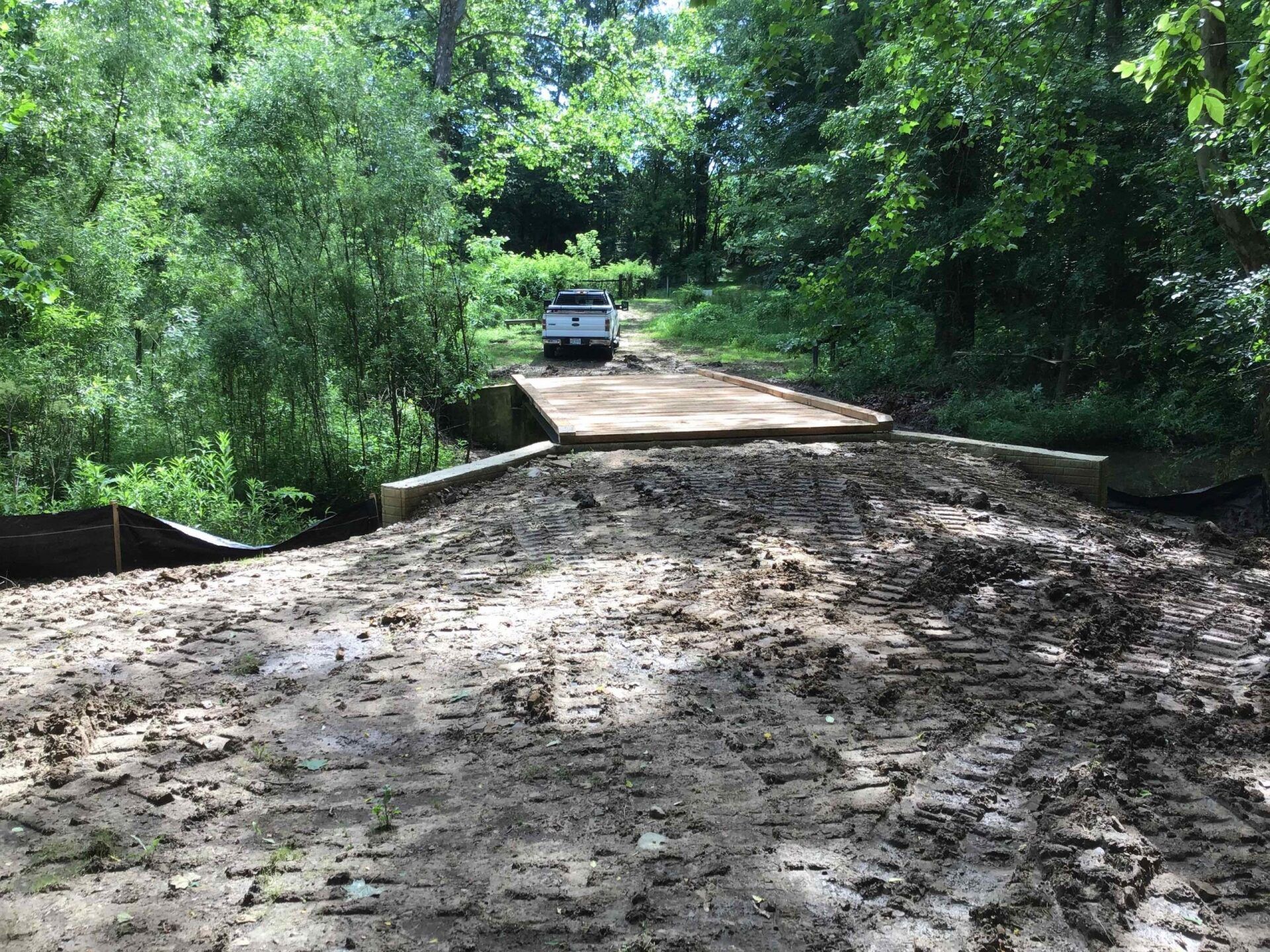 A truck is driving over a muddy bridge in the woods.