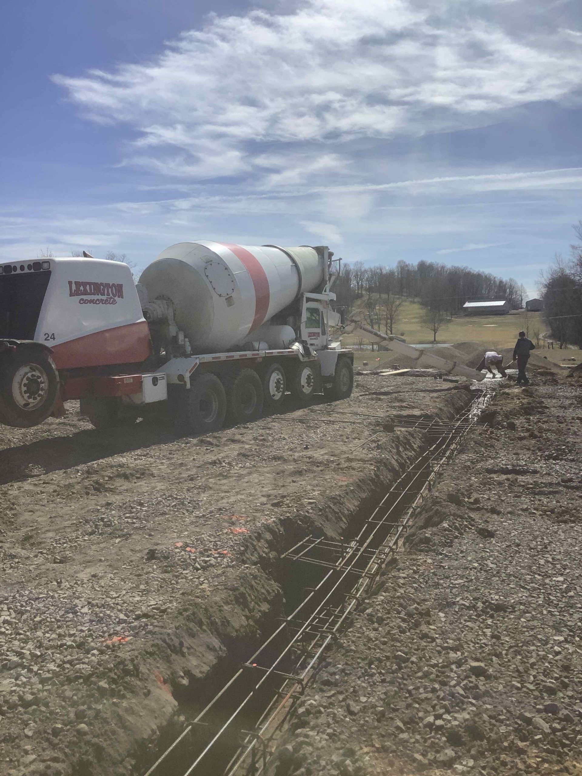 A concrete mixer truck is driving down a dirt road.