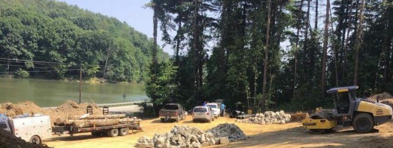 A construction site in the middle of a forest next to a lake.