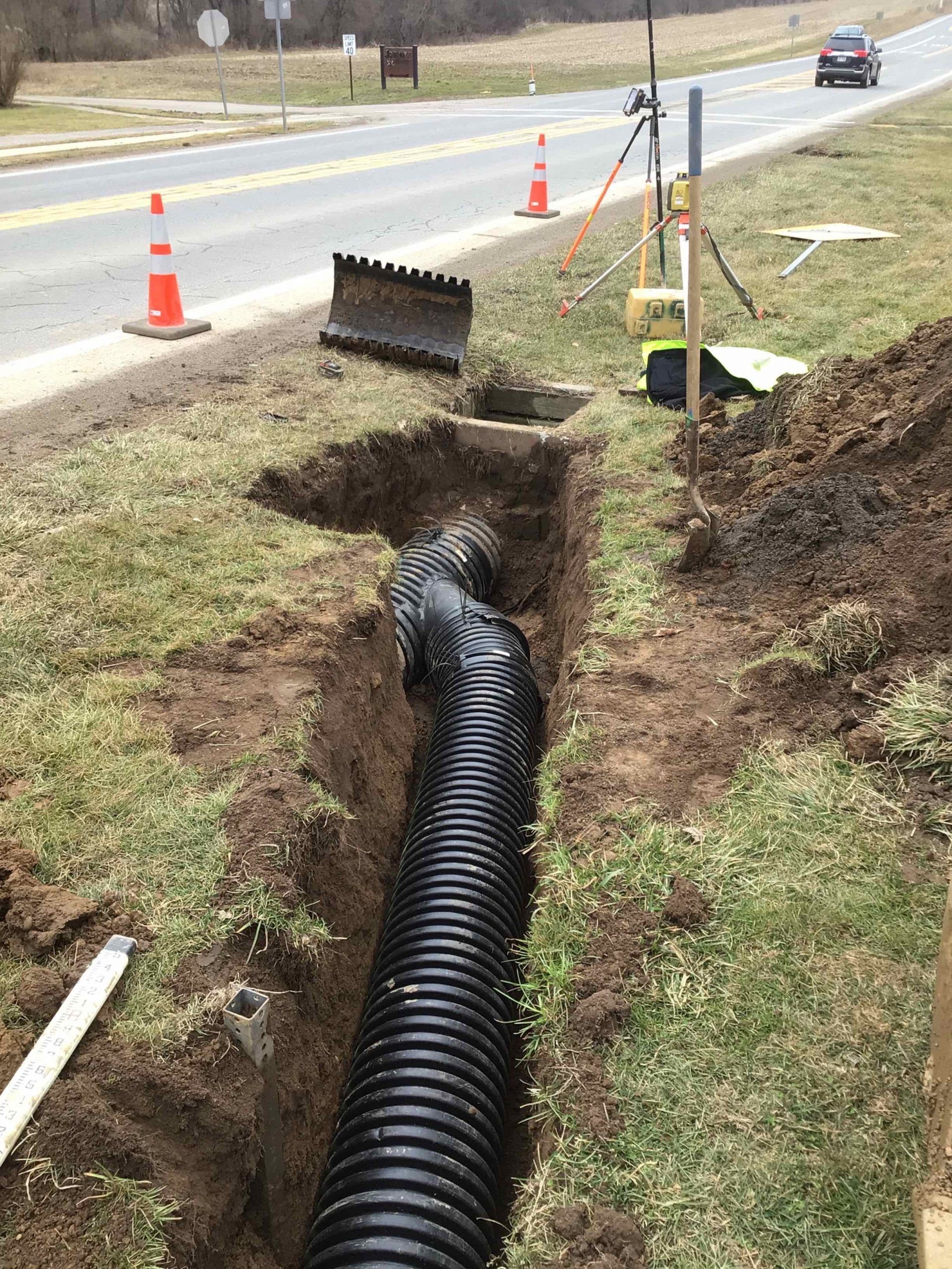 A large black pipe is being installed in a trench next to a road.