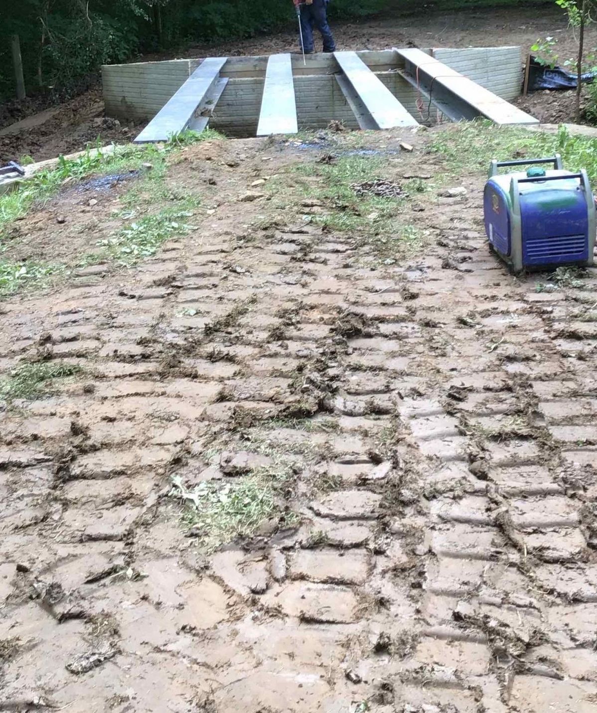 A blue generator is sitting on a muddy brick road.