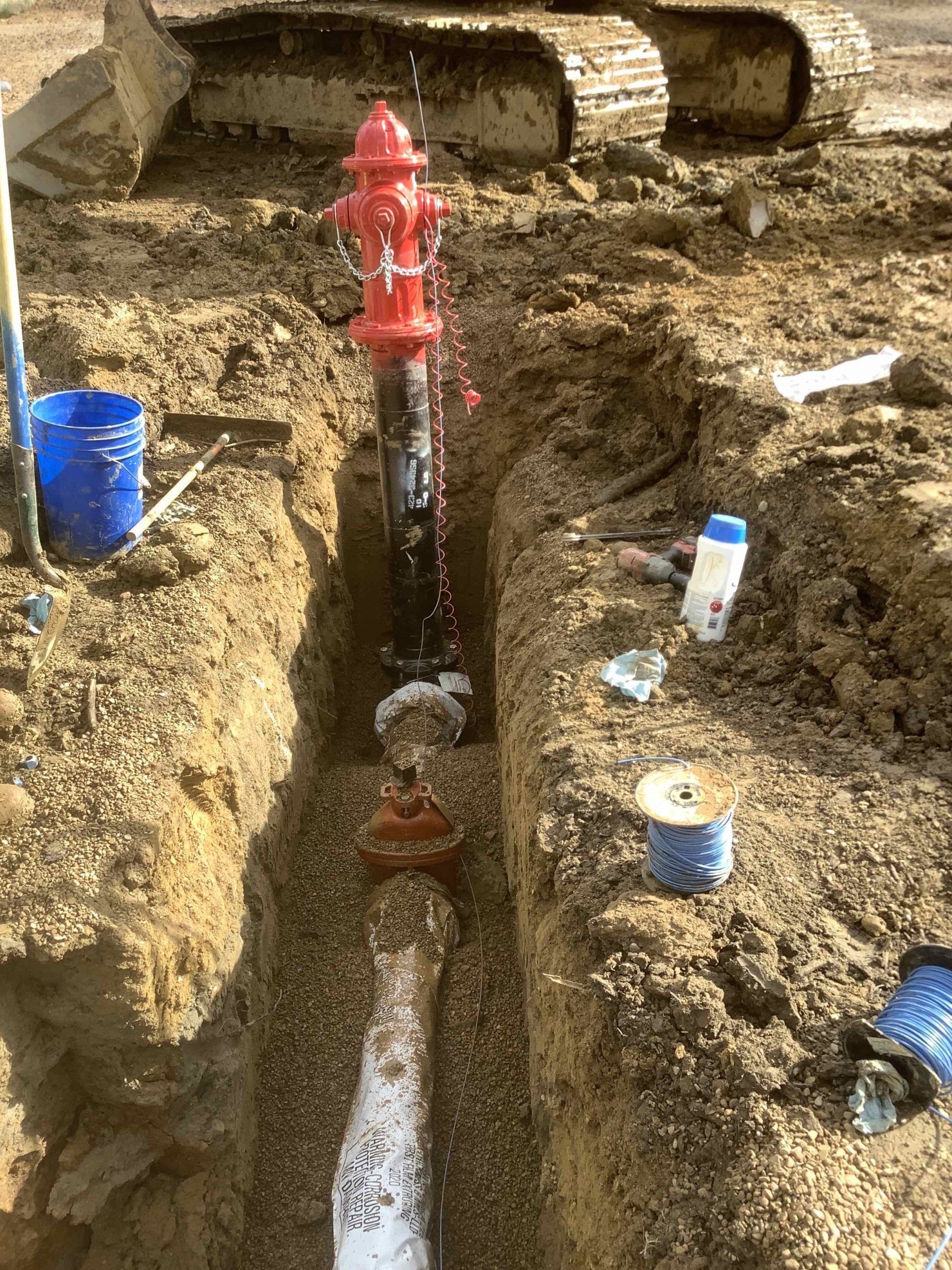 A red fire hydrant is sitting in the dirt next to a white pipe.