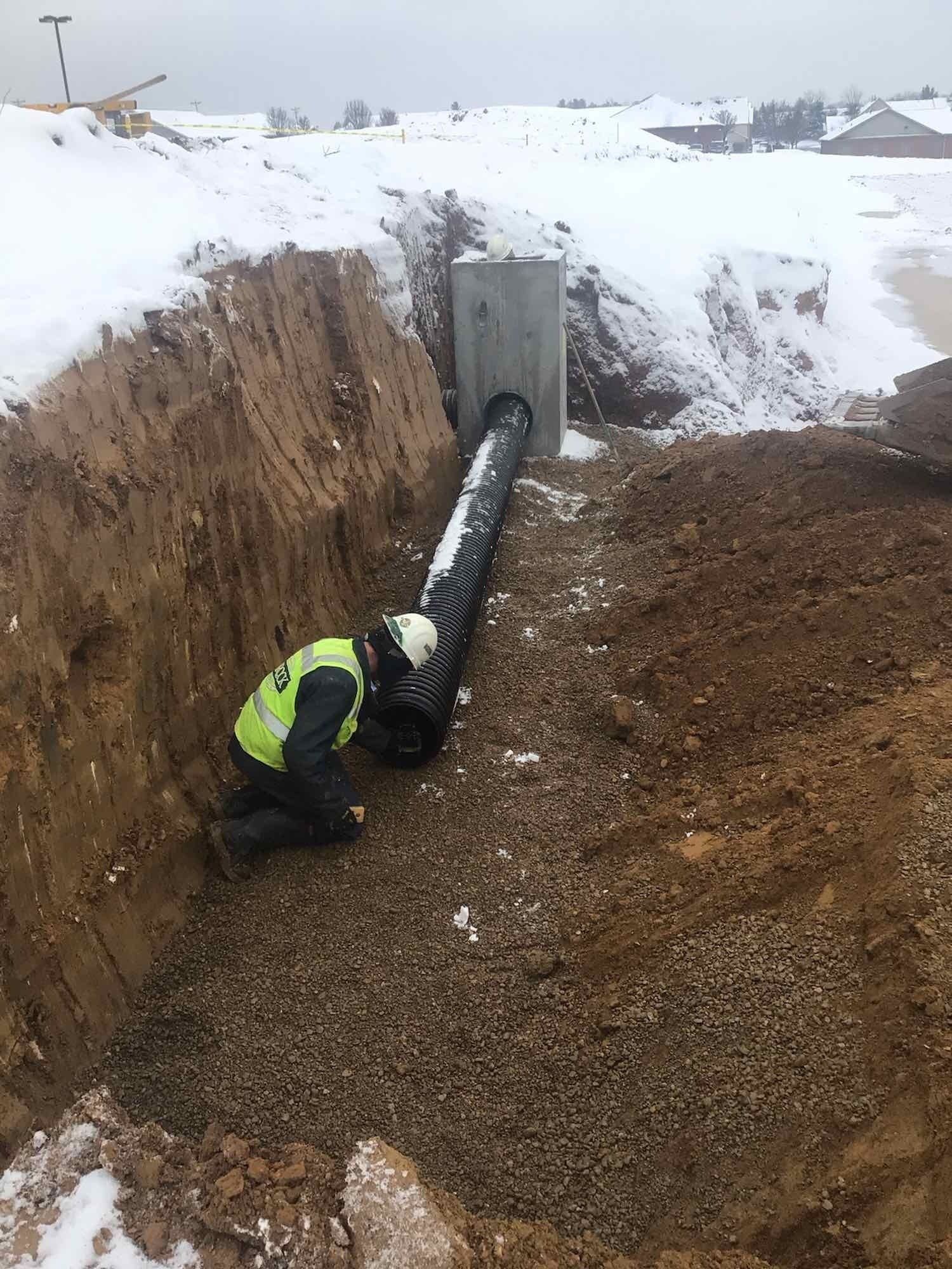 A man is kneeling in the dirt next to a pipe.